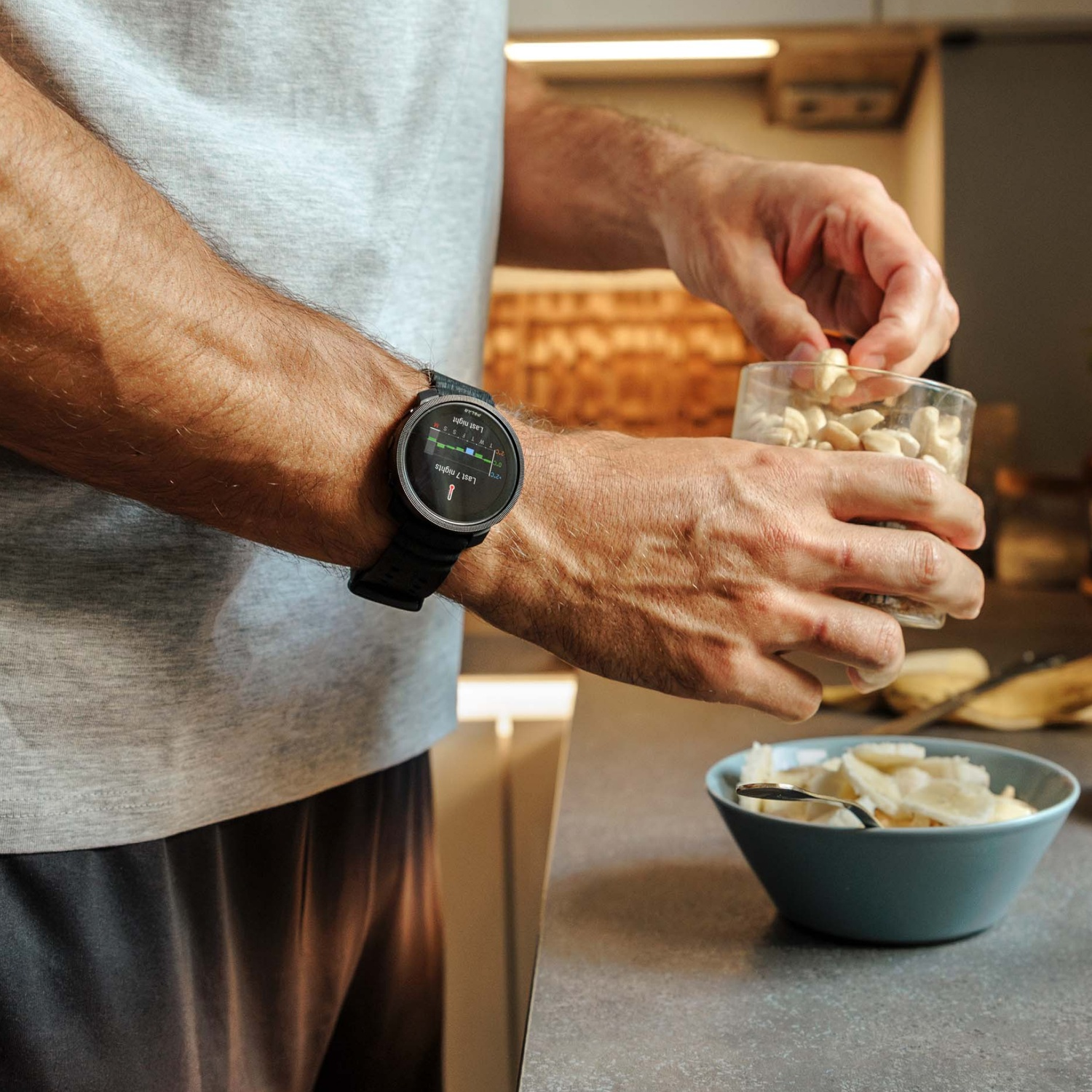 Een man met een smartwatch houdt een glas noten en een kom met gesneden bananen vast.