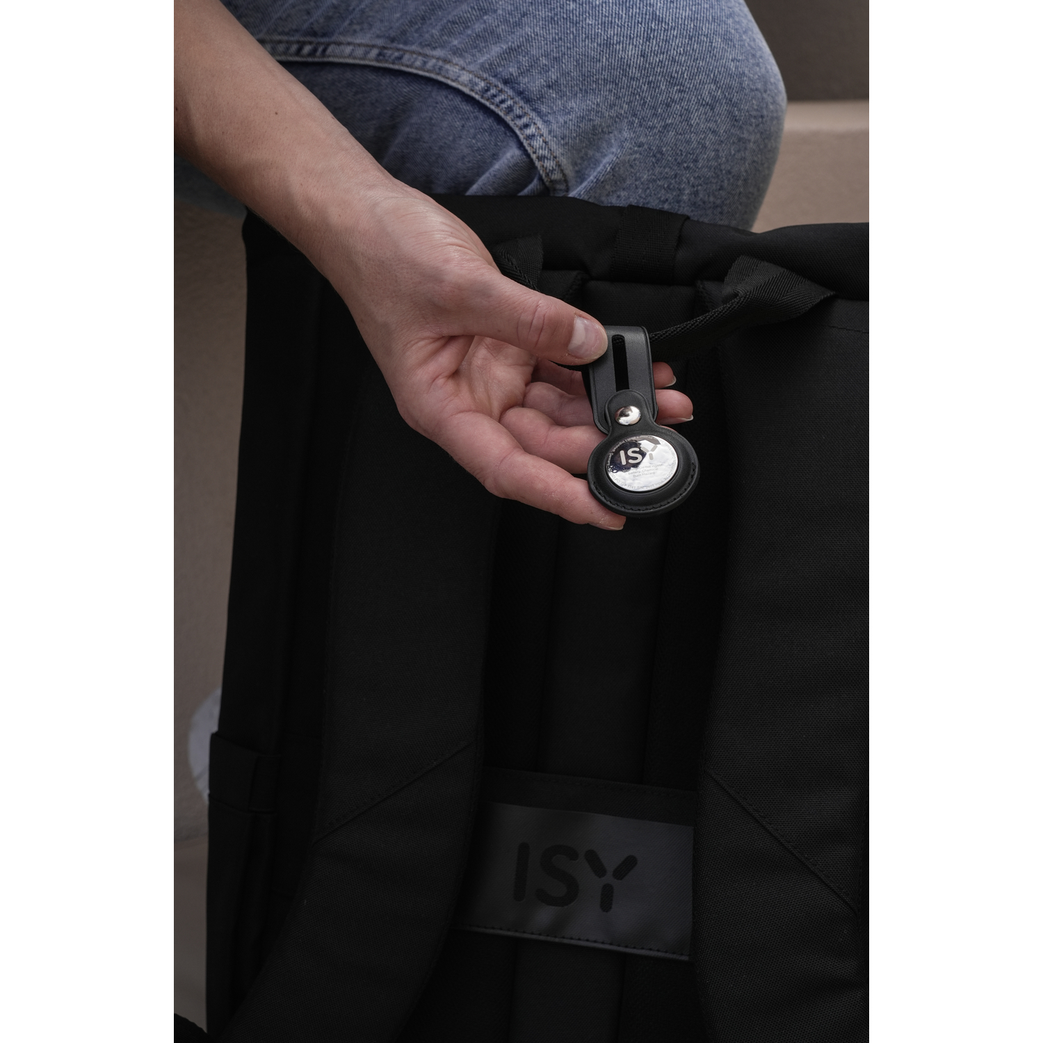 A person attaching a black AirTag to a backpack.