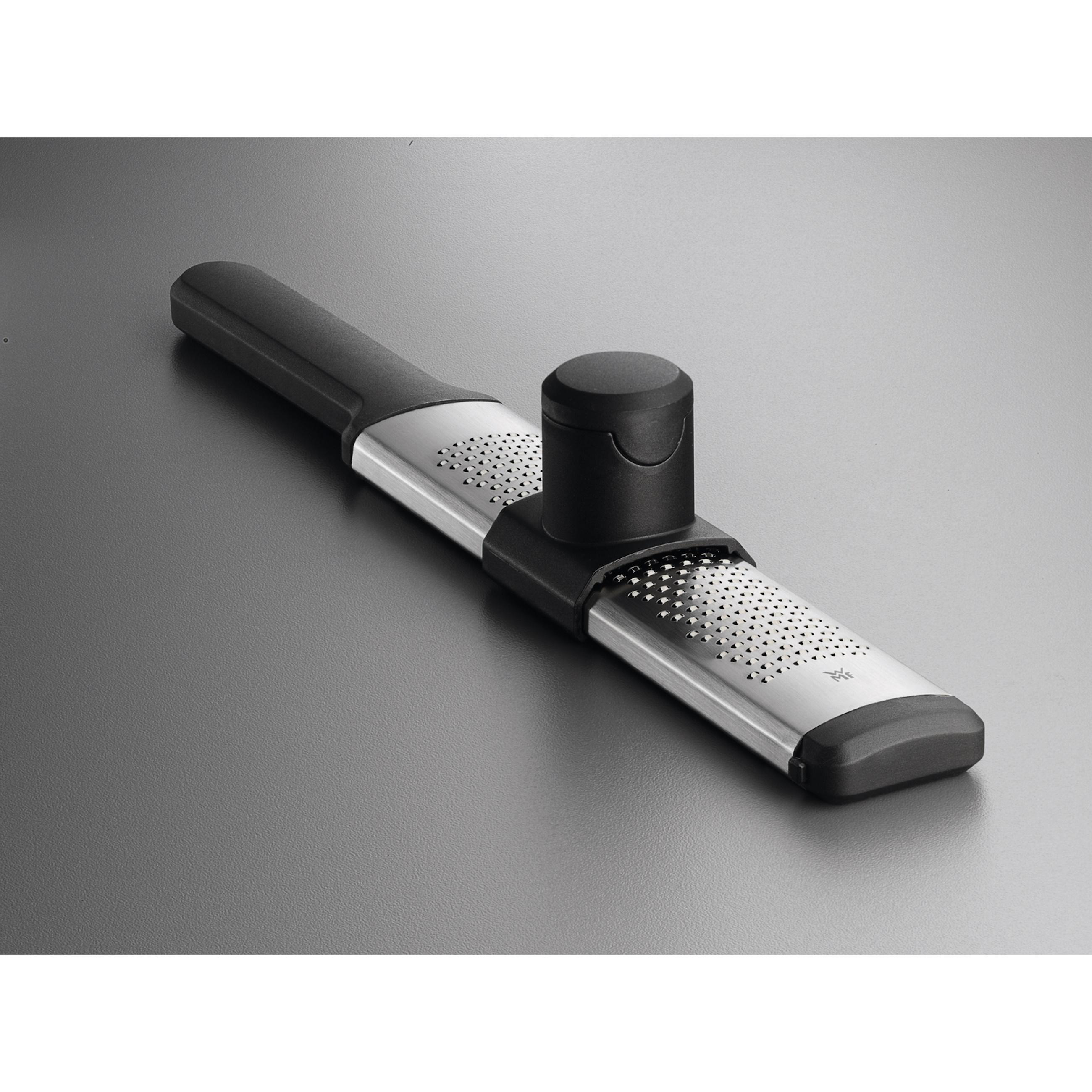 Ein silberner Küchenreibe mit schwarzem Griff und schwarzer Kappe auf grauer Oberfläche.