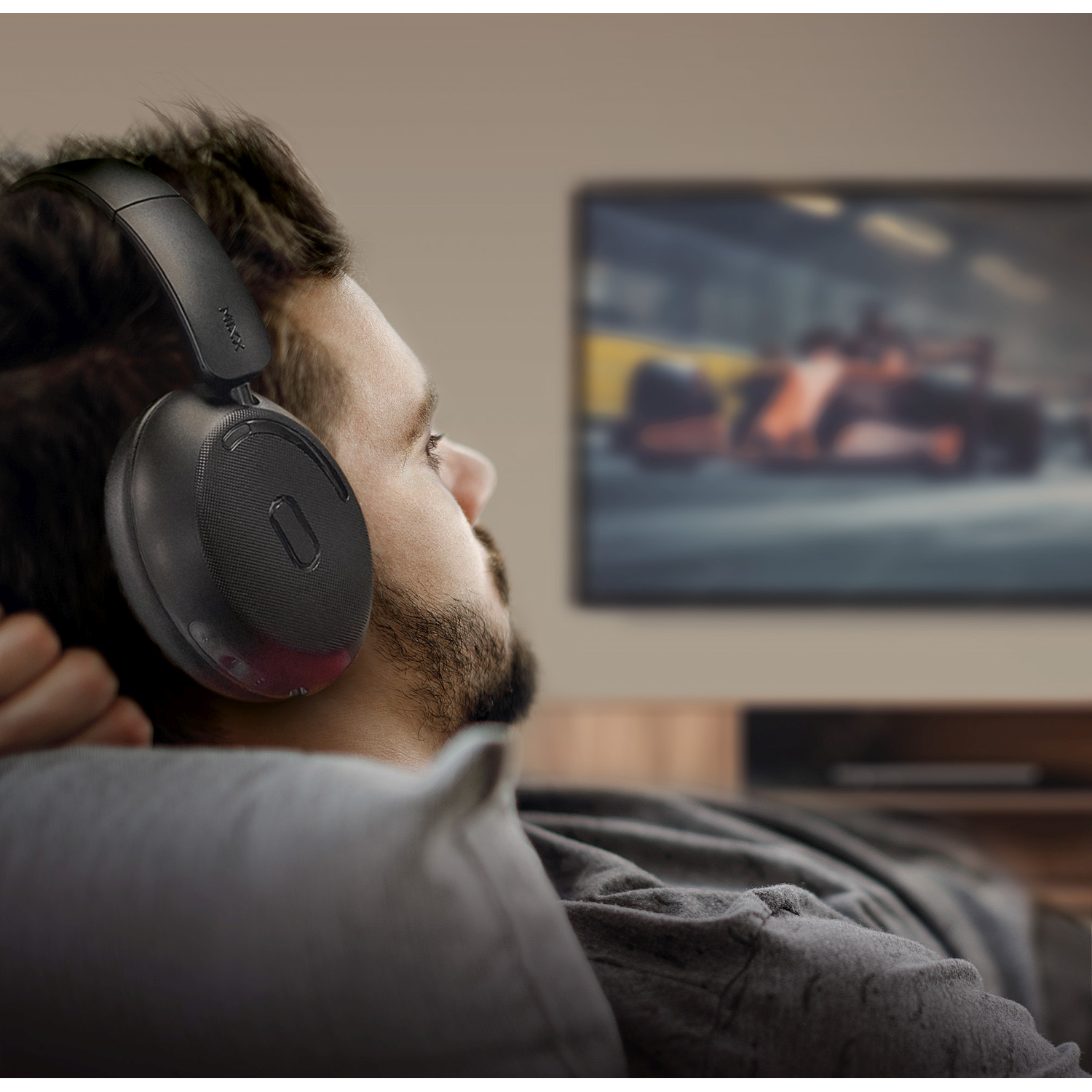 Man wearing headphones watches TV. The screen shows a blurred race car. He is relaxing on a sofa.