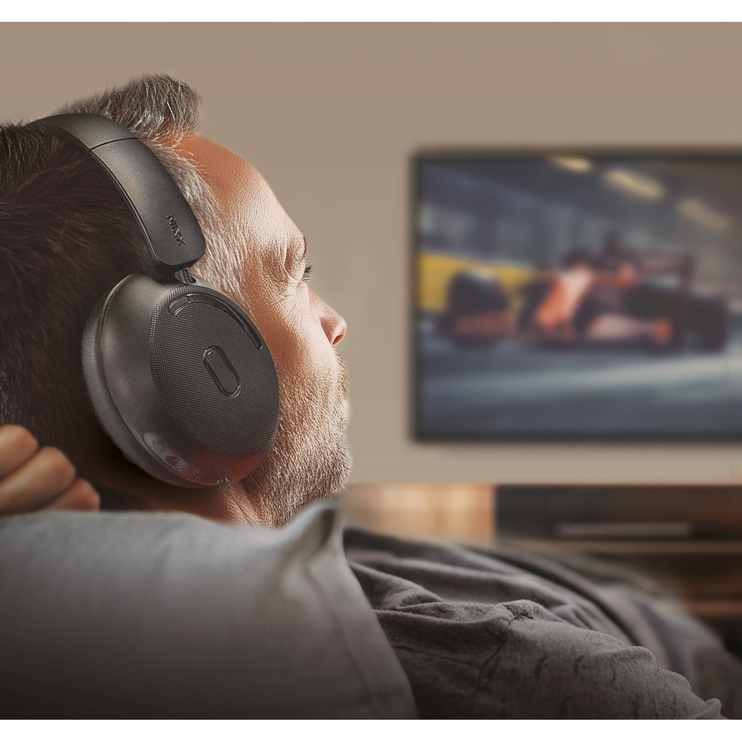 Man wearing headphones, watching TV with a blurry race car image. He is sitting, indoors.