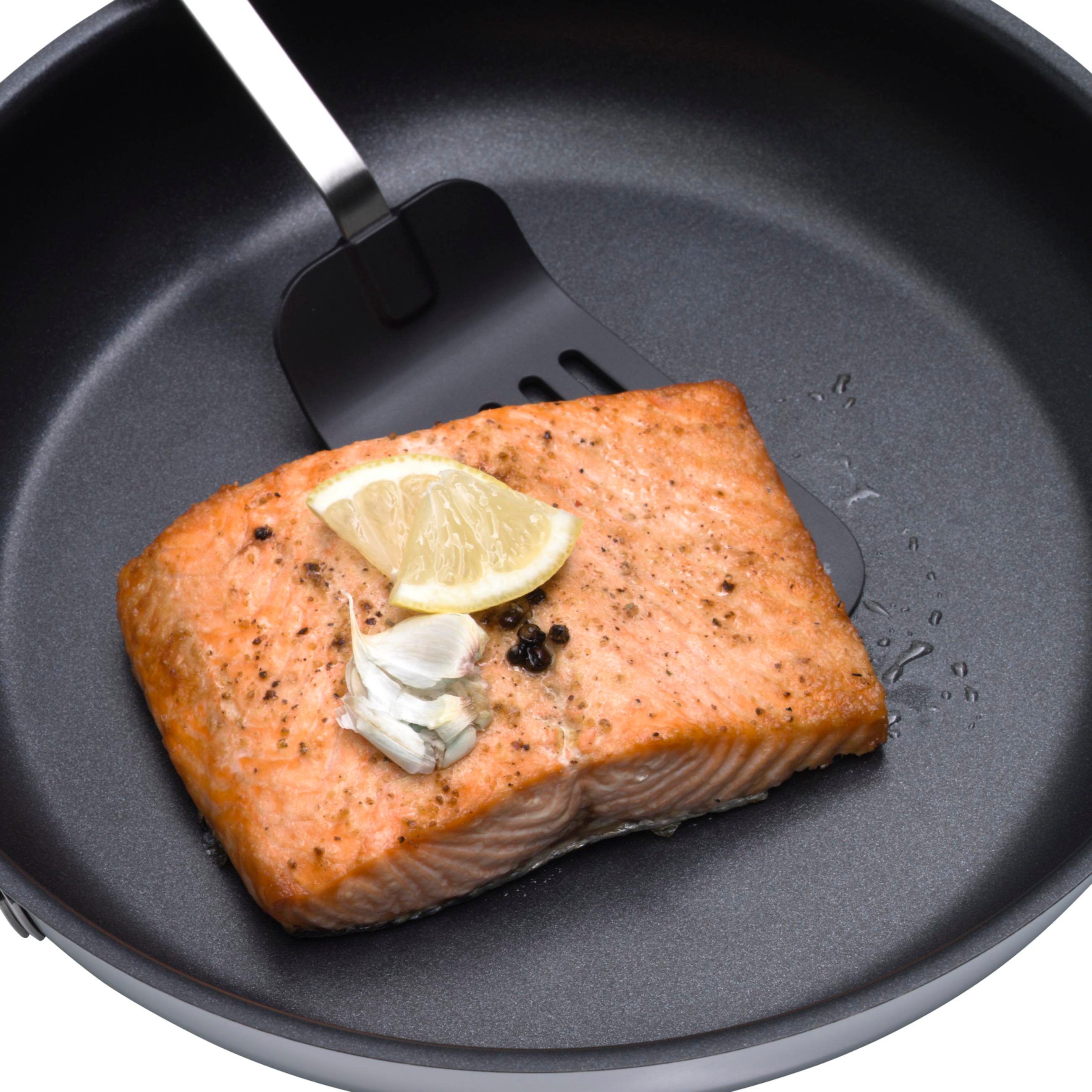 Lachsfilet in der Pfanne mit Zitrone und Knoblauch. Schwarze Pfanne. Weißer Hintergrund.