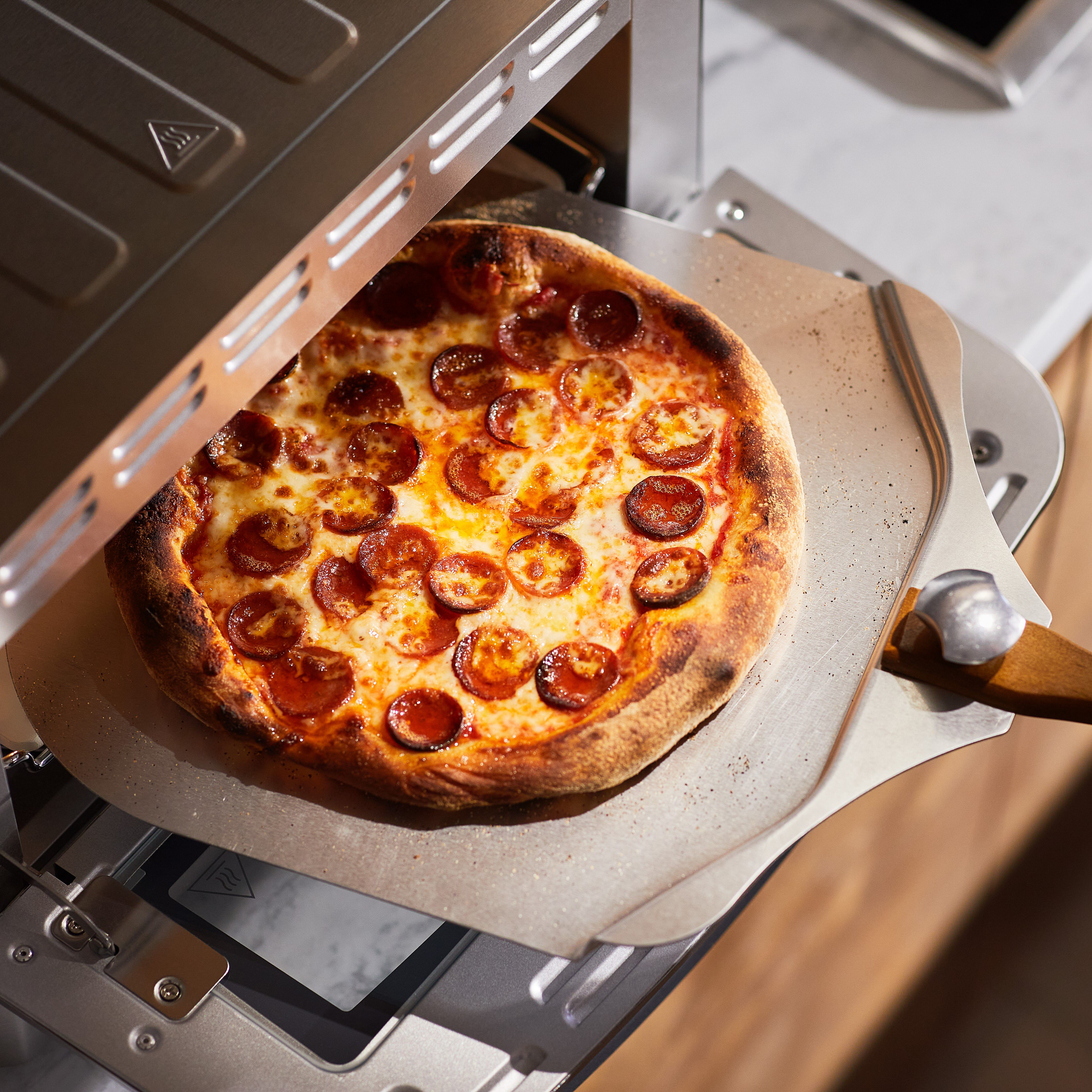 Une pizza au pepperoni est dans un four. Une pelle à pizza en métal est à côté.