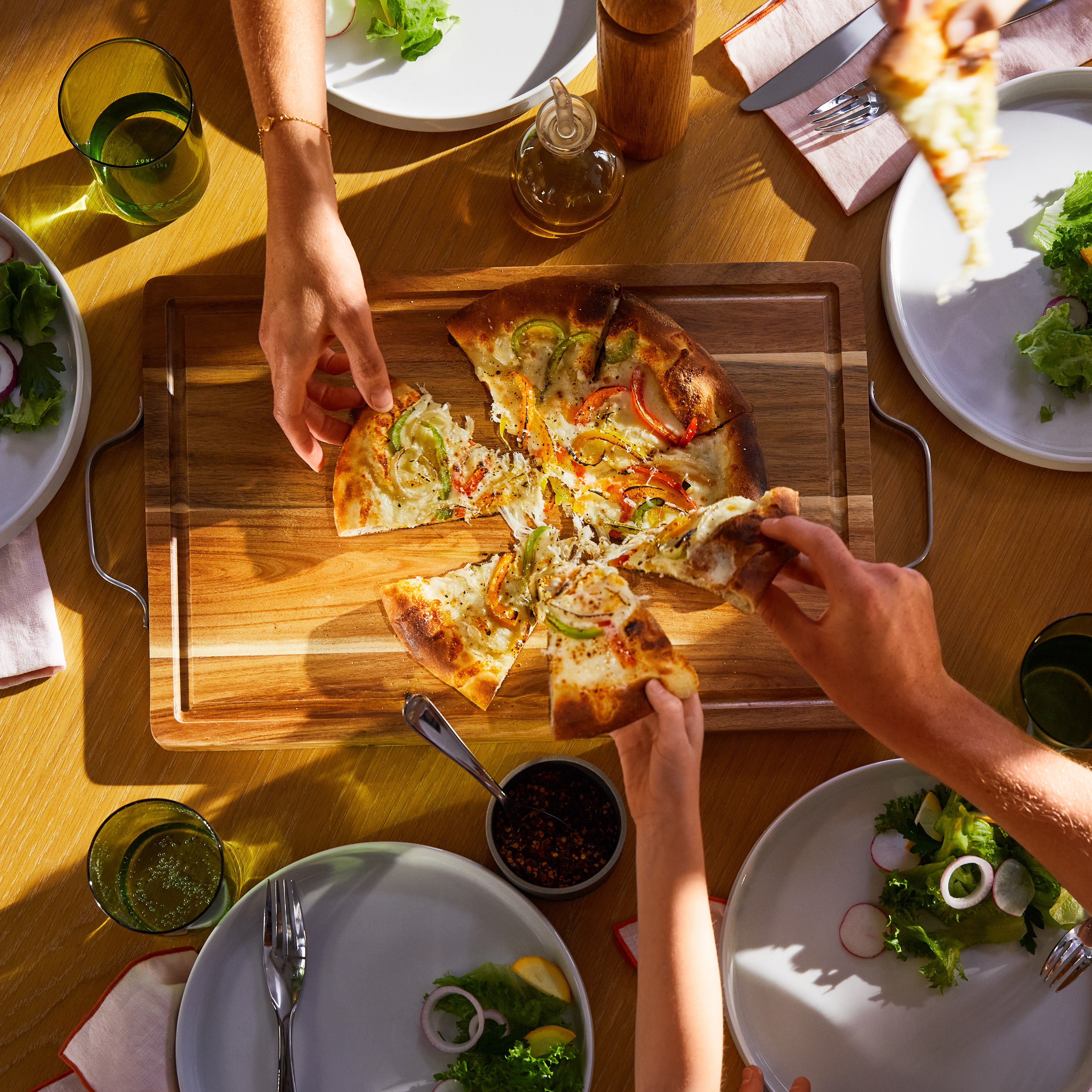 Des gens partagent une pizza, une salade et des boissons sur une table en bois, vue aérienne.