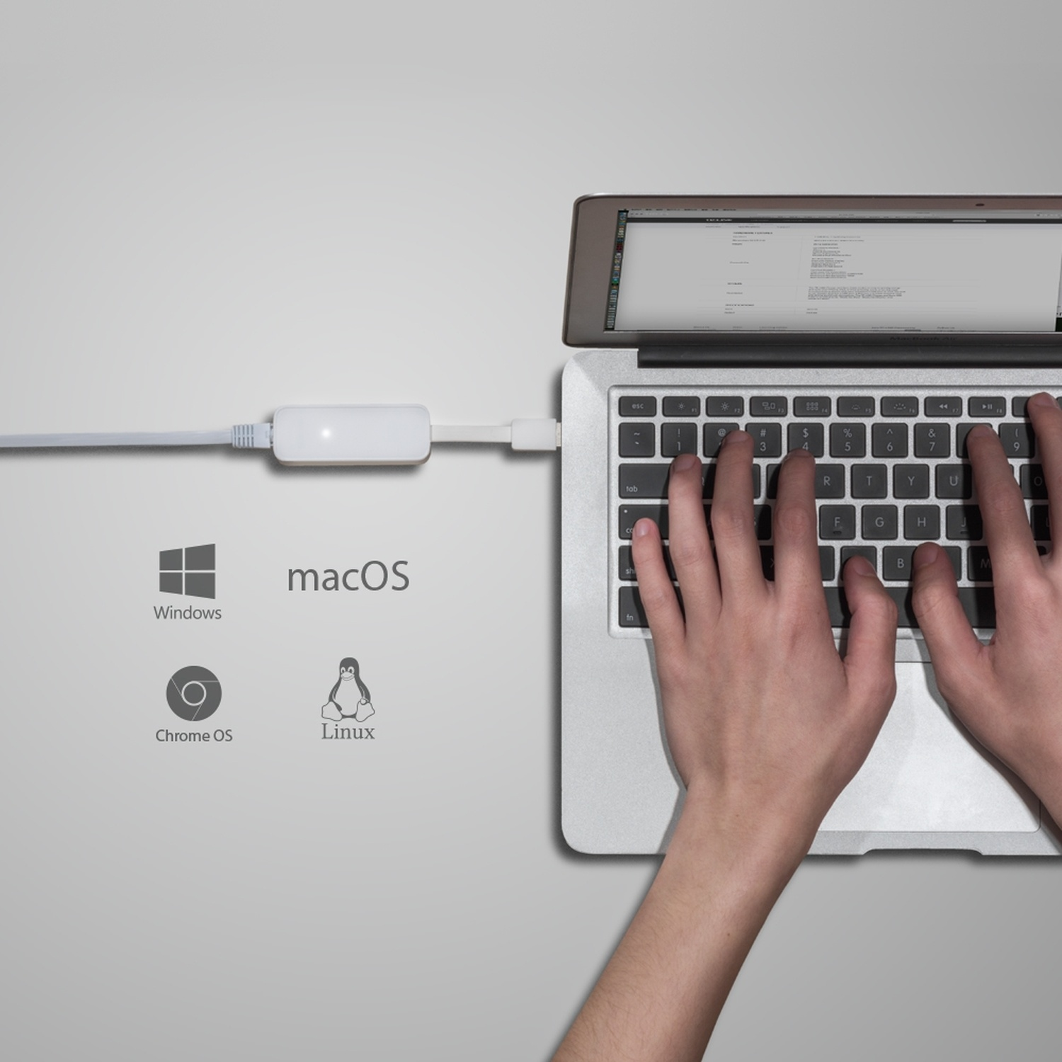 Mani su una tastiera di un laptop, collegata a un cavo bianco e macOS.