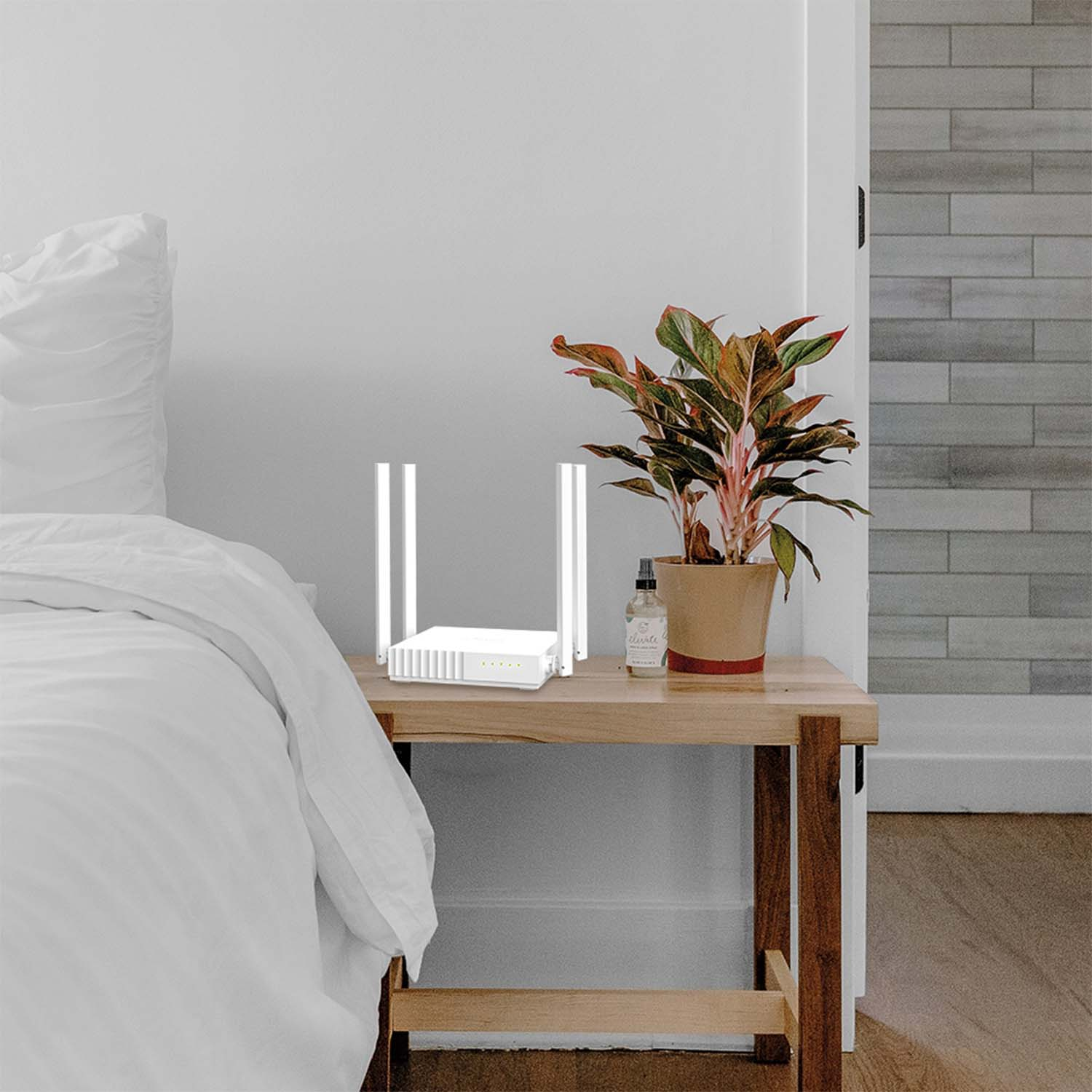 Un router bianco con due antenne e una pianta in vaso su un tavolo di legno.