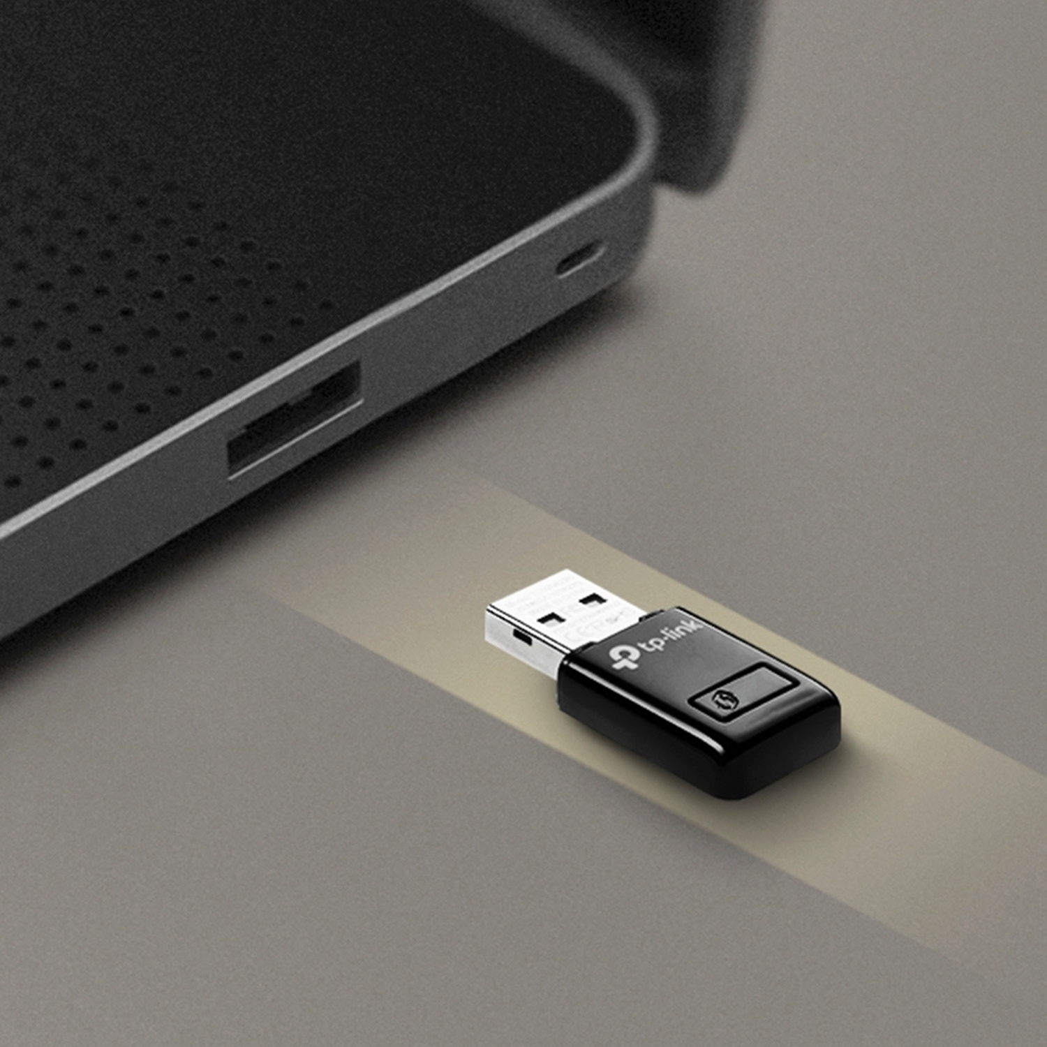 Un adattatore Wi-Fi USB nero è collegato a un laptop, su una superficie grigia.