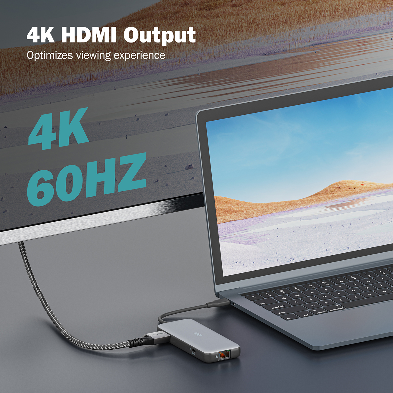 Ein Laptop, der mit einem silbernen Hub verbunden ist. Der Text auf dem Bildschirm lautet 4K 60HZ. Verschwommene Landschaft.