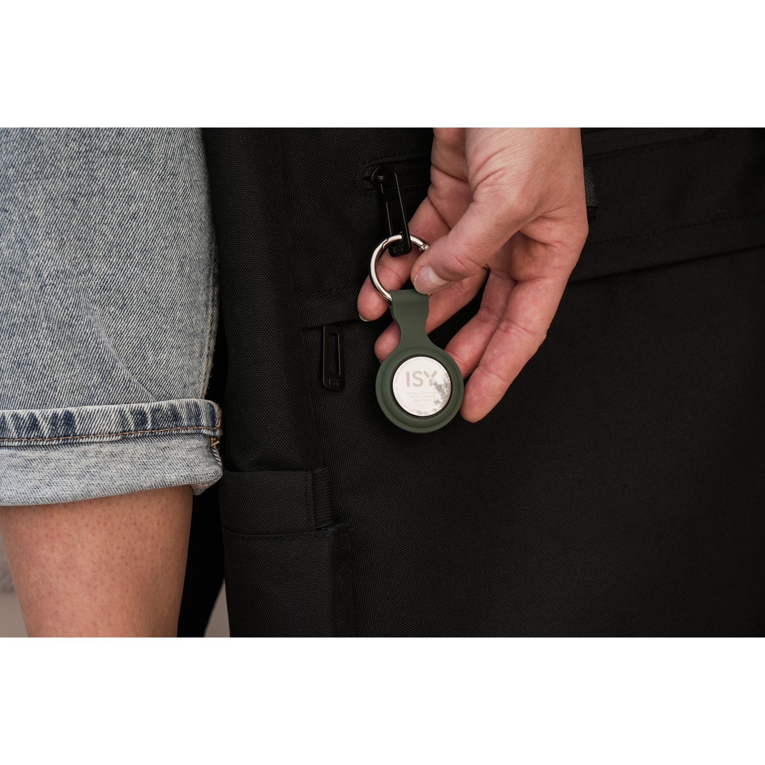 Hand holding a small, dark green circular device with a key ring, on a black background.