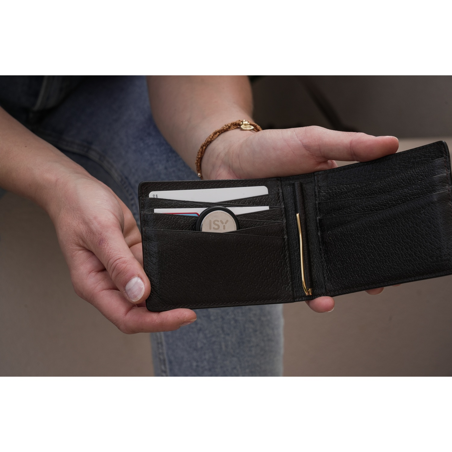 A person's hands holding a black wallet open, revealing cards and a tracking device.