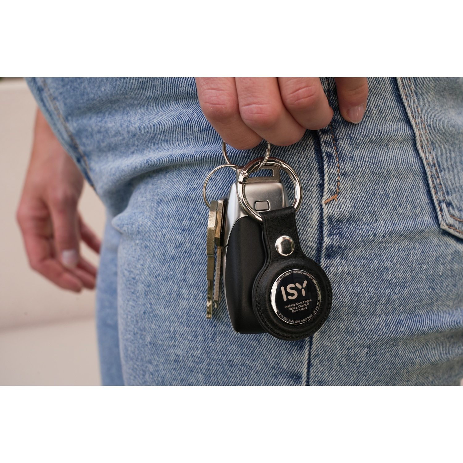 A hand holding a keyring with keys, and a black ISY tag. A pair of jeans.