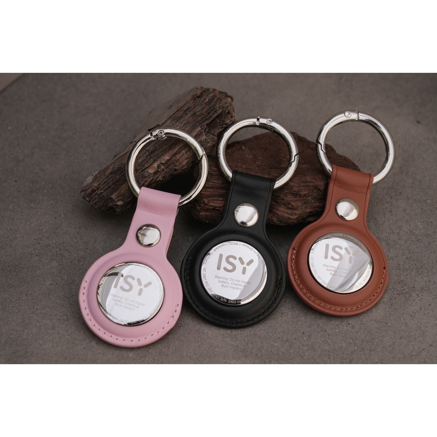 Three keychains with circular tags in pink, black, and brown, on a rock.