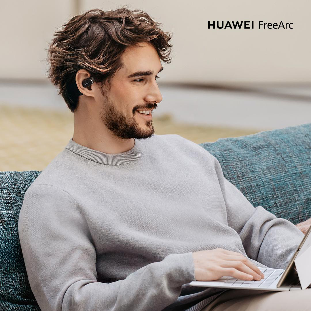 Ein Mann mit Ohrhörern sitzt auf einem Sofa und benutzt einen Laptop. Er lächelt. Das Bild hat ein HUAWEI FreeArc Logo.