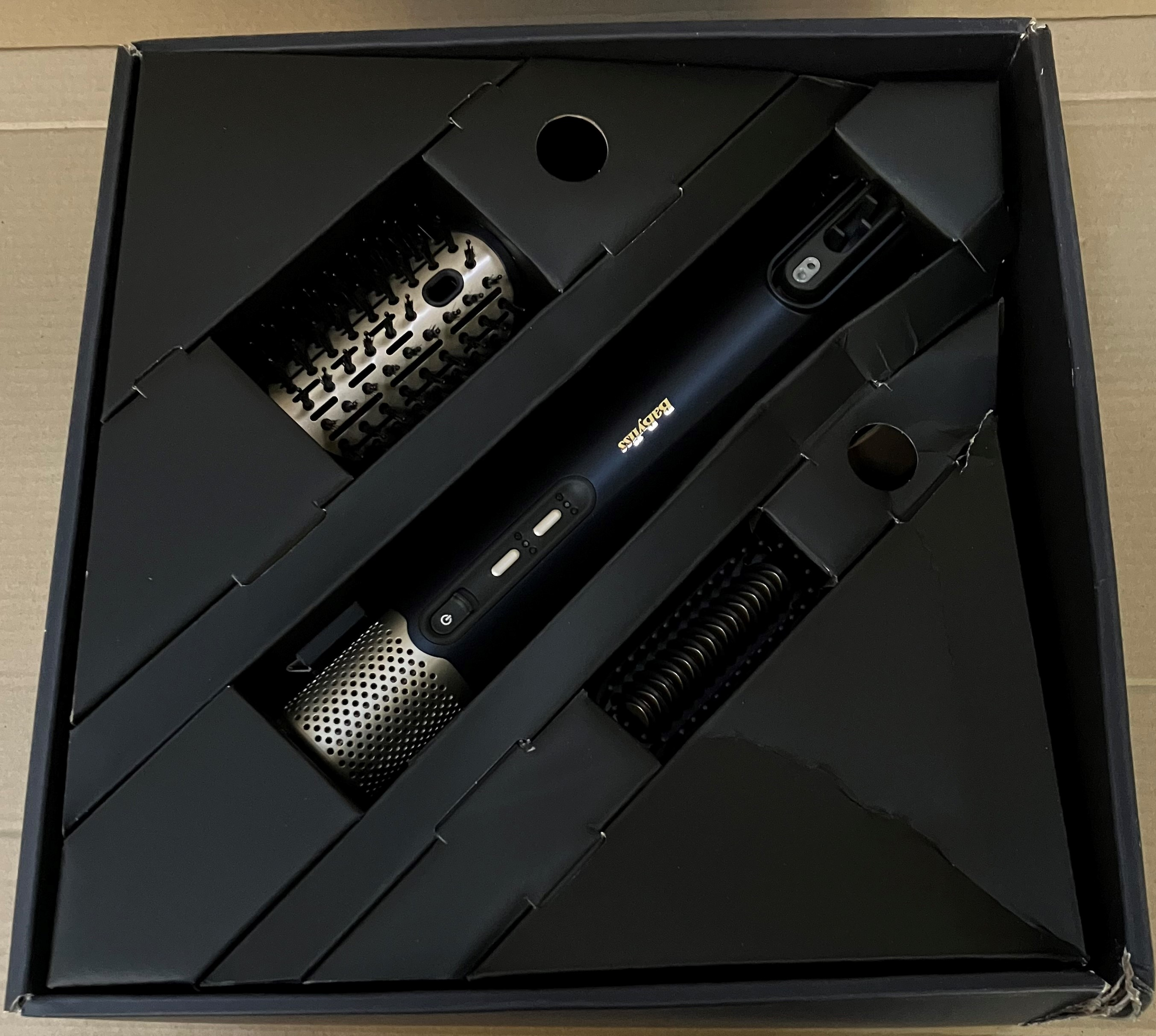 Czarne pudełko zawiera czarną suszarkę do włosów z nasadkami.