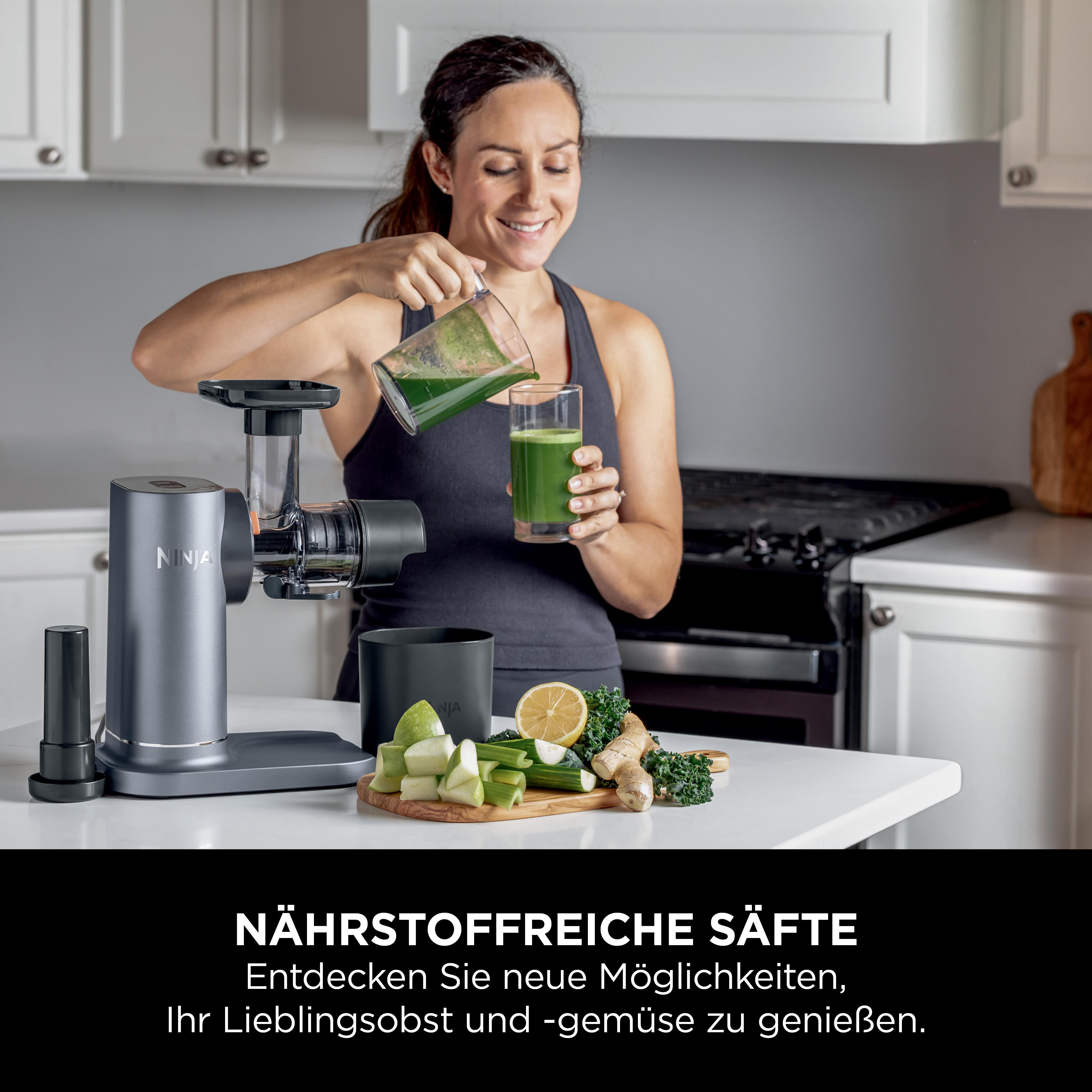 Eine Frau gießt Saft in ein Glas neben einer Saftpresse auf einem Tisch.
