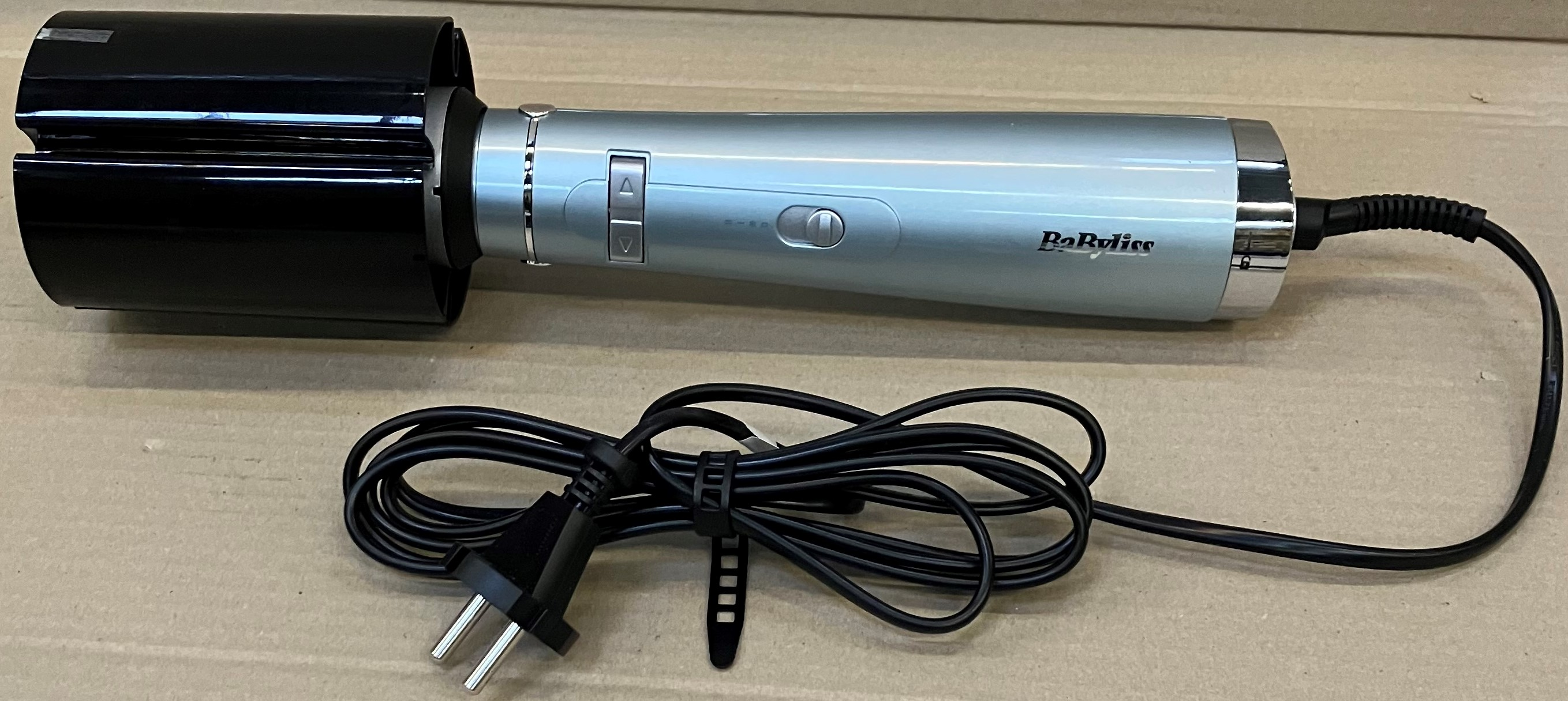 Srebrna lokówka z czarną końcówką i kablem na kartonie.