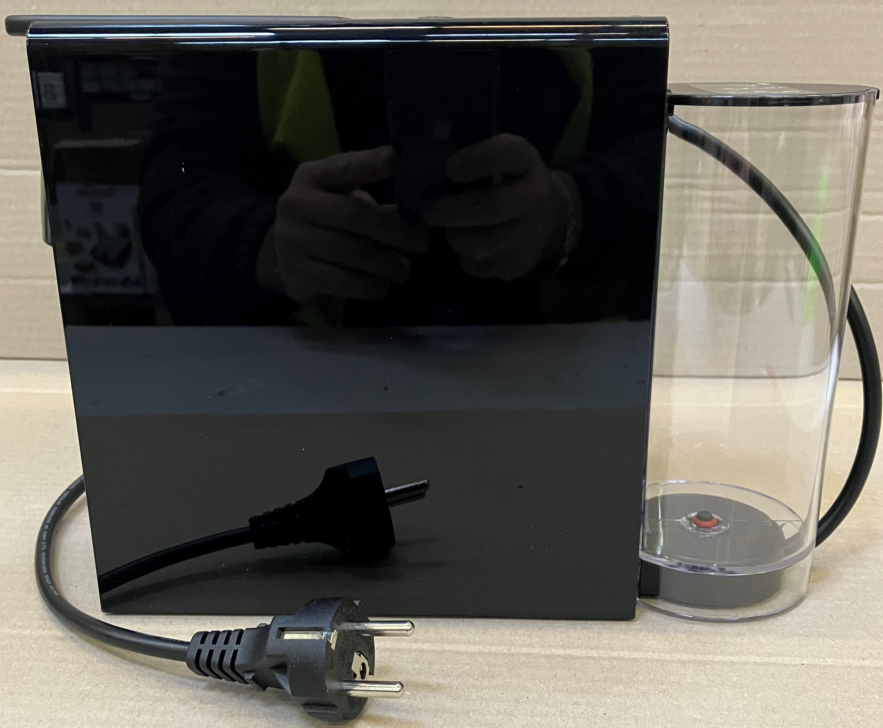 Czarne urządzenie z wtyczką i przezroczystym pojemnikiem na wodę.