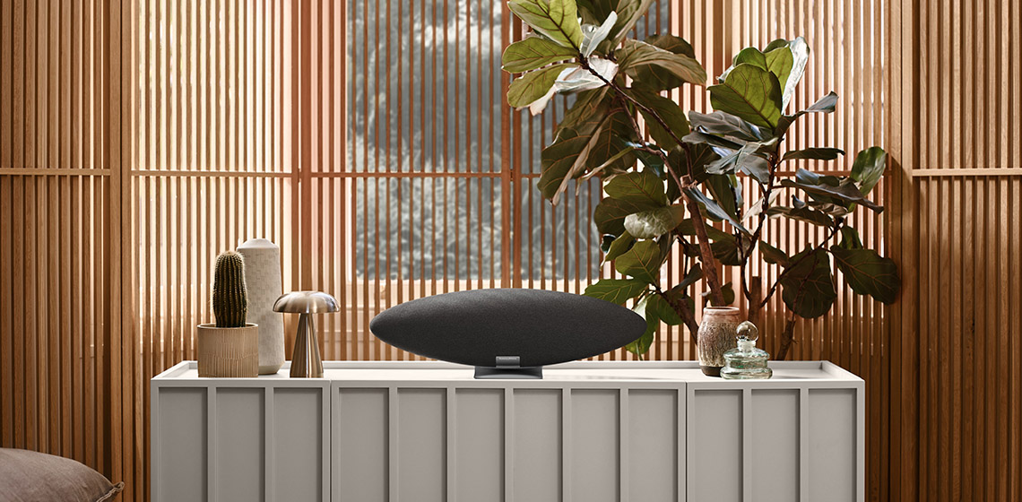 Nowoczesny salon z głośnikiem na szafce, roślinami i drewnianymi panelami ściennymi.