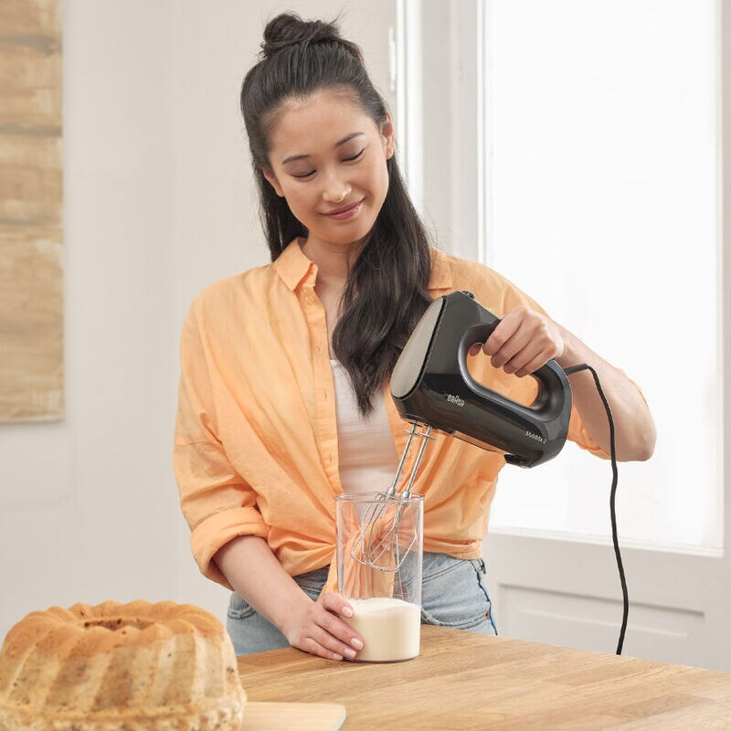 Kobieta używa miksera ręcznego Braun do mieszania składników w szklance. Obok znajduje się ciasto.