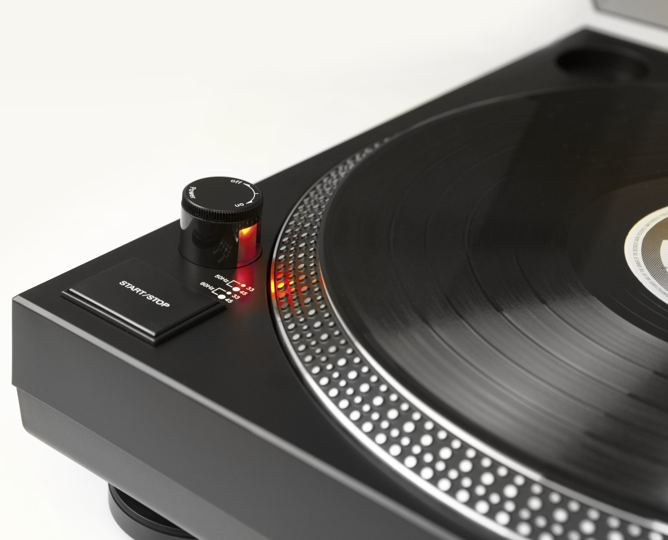 Zbliżenie czarnego gramofonu. Płyta winylowa, elementy sterujące. Przycisk zasilania świeci się na czerwono.