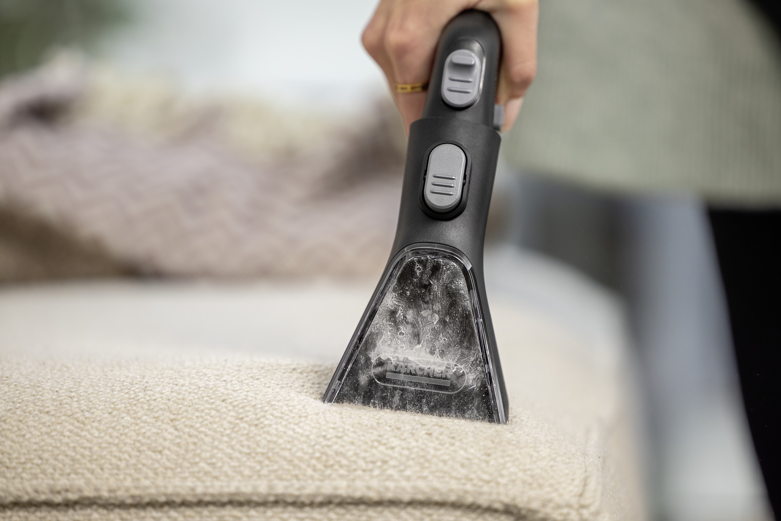 Dłoń używająca głowicy odkurzacza na beżowej sofie, zbliżenie.