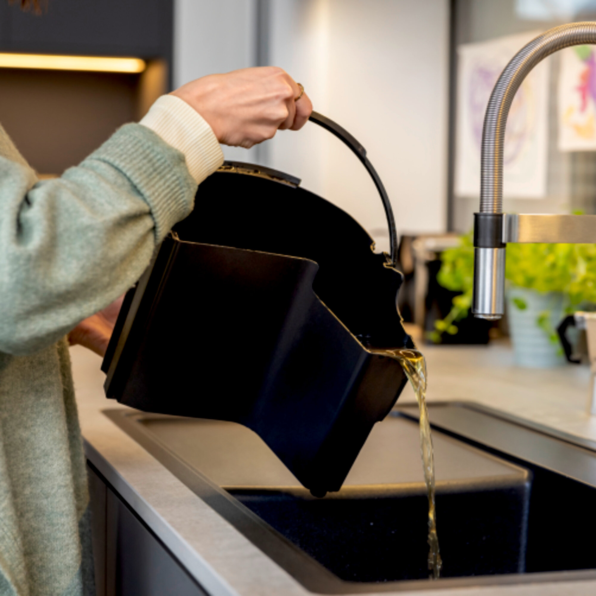 Osoba wylewa płyn z czarnego pojemnika do zlewu.