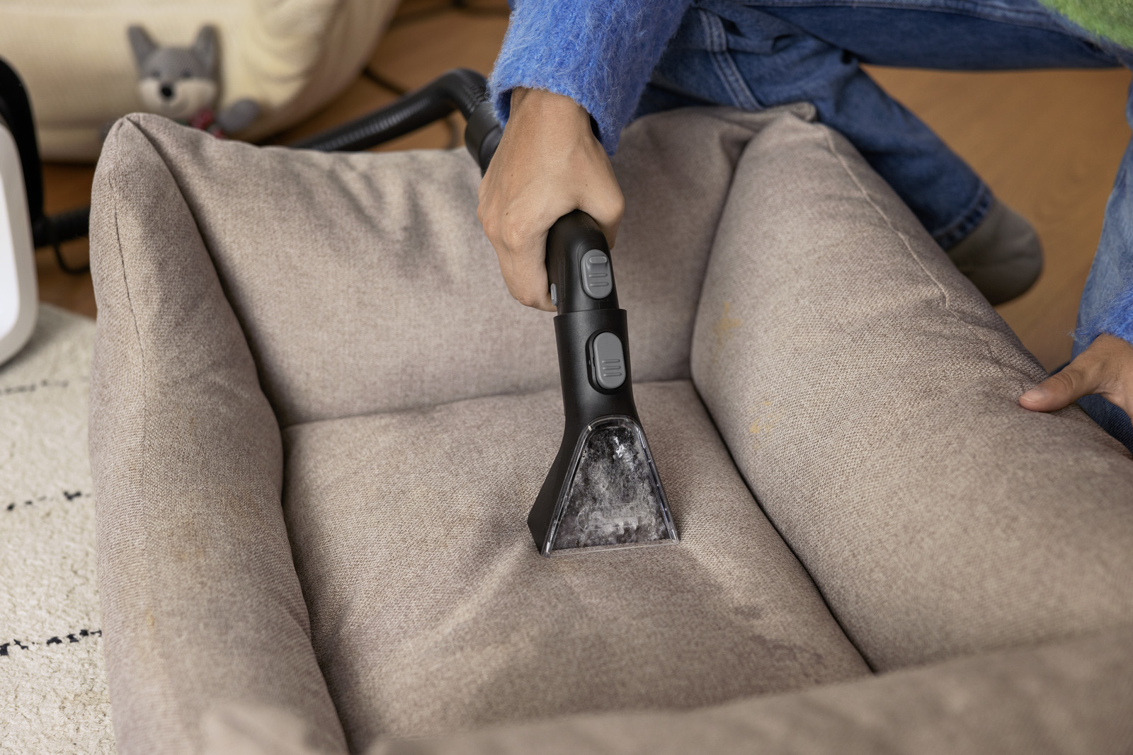 Osoba czyszcząca legowisko dla psa za pomocą dyszy odkurzacza.