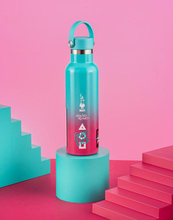 Eine türkisfarbene Wasserflasche auf einem türkisfarbenen Ständer, mit pinkem Hintergrund und Treppen.
