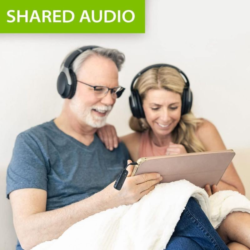 Couple de personnes âgées partageant de l'audio depuis une tablette, tous deux portant des écouteurs, souriant. Texte 'SHARED AUDIO'.