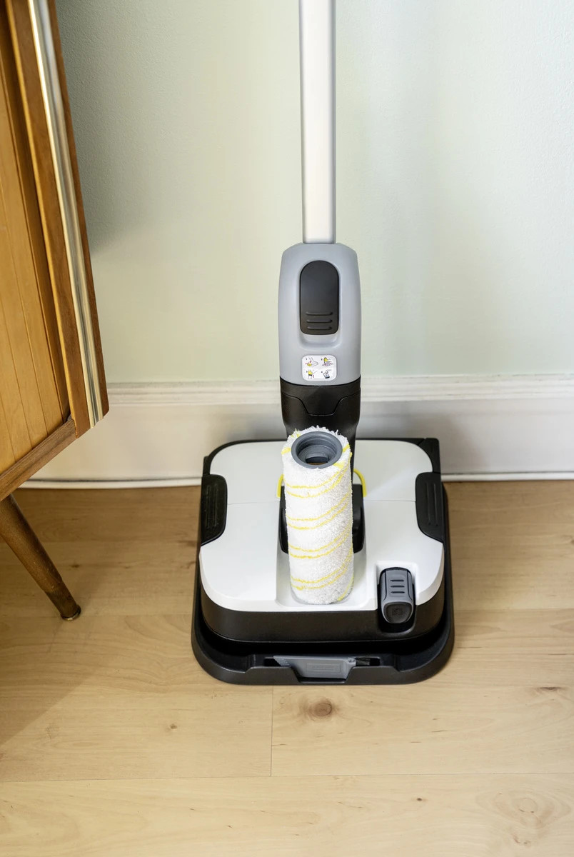 Biało-czarna myjka do podłóg z wałkiem, na drewnianej podłodze, ze ścianą i szafką.