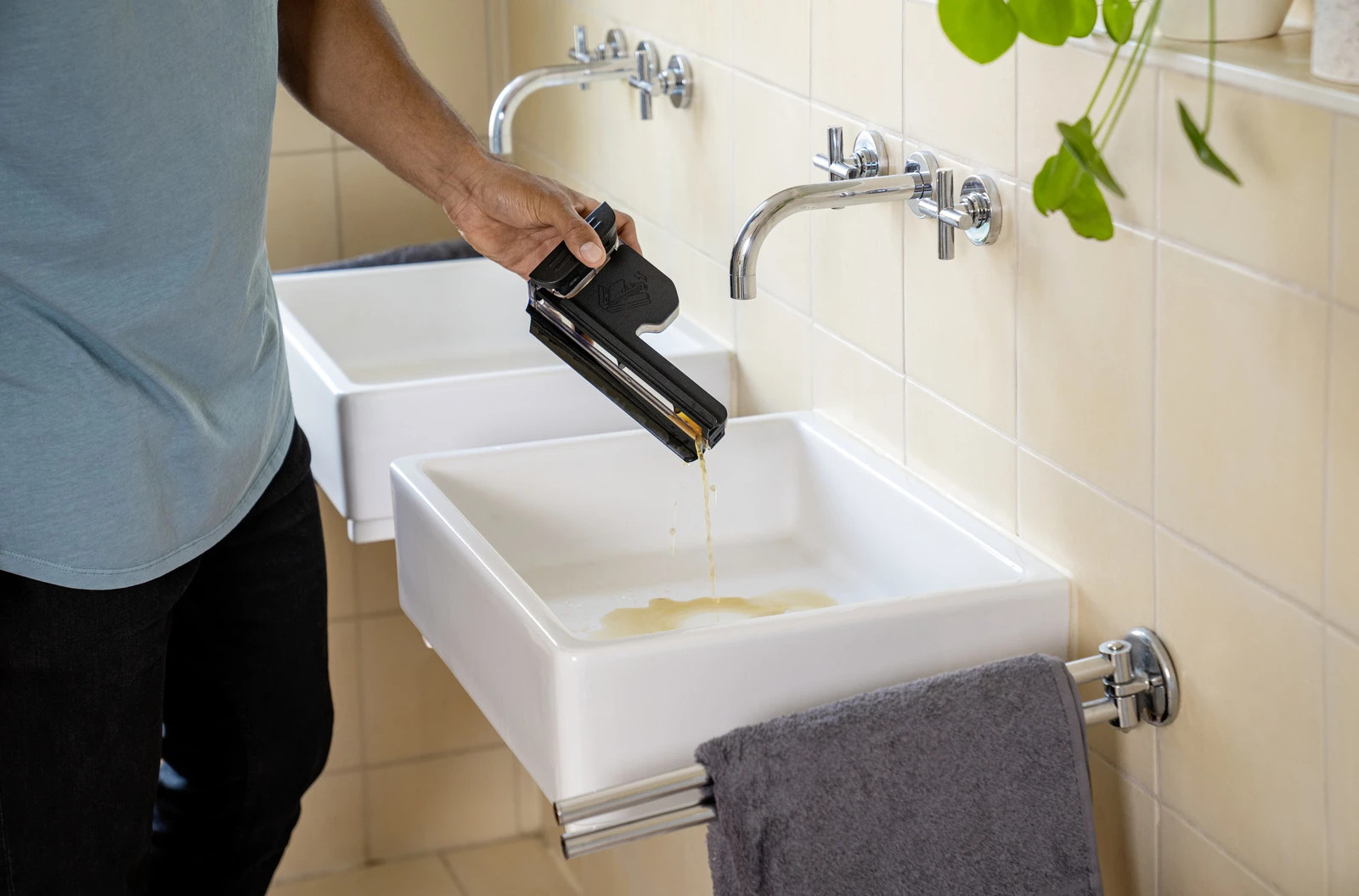 Osoba wylewająca ciecz z czarnego narzędzia do białego zlewu, w pobliżu kranu.