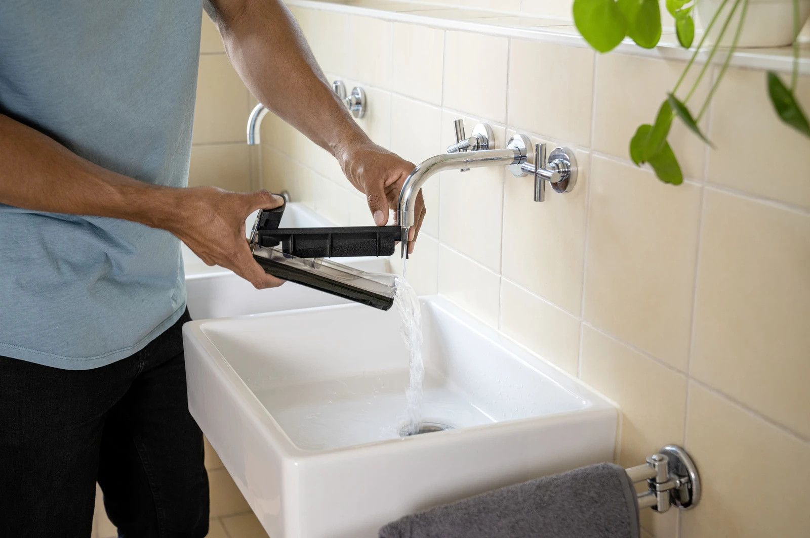 Osoba płucze czarny filtr pod bieżącą wodą w białym zlewie. Otoczenie łazienki.