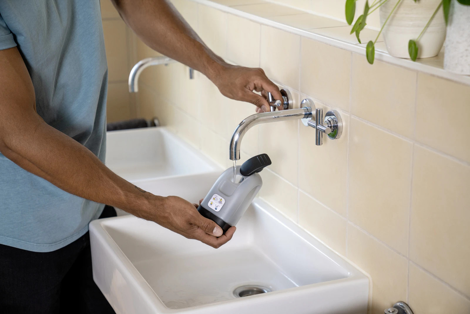 Osoba napełnia szary pojemnik pod kranem w umywalce w łazience.
