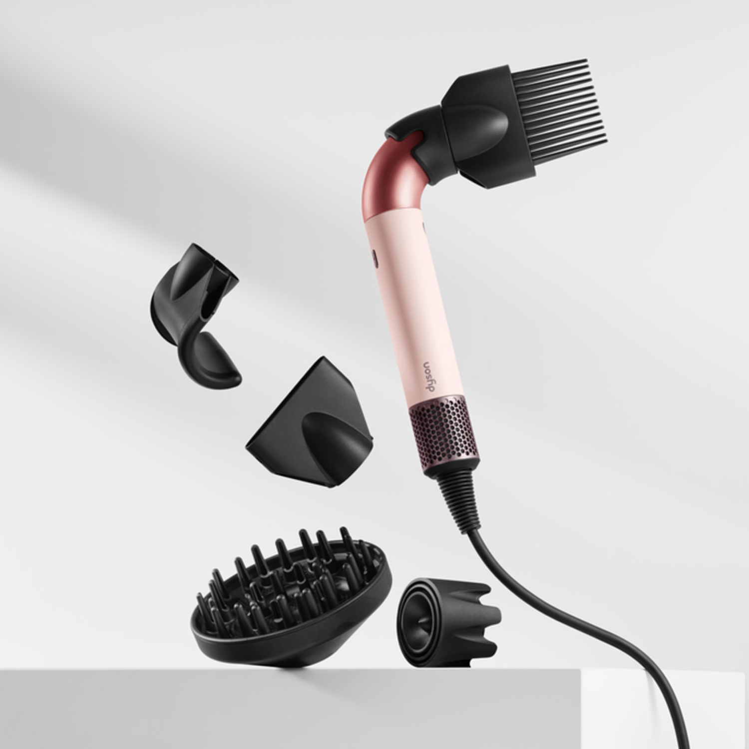 Dyson haarstylingtool en accessoires. Roze en zwart kleurenschema. Witte achtergrond, zwevend in de lucht.