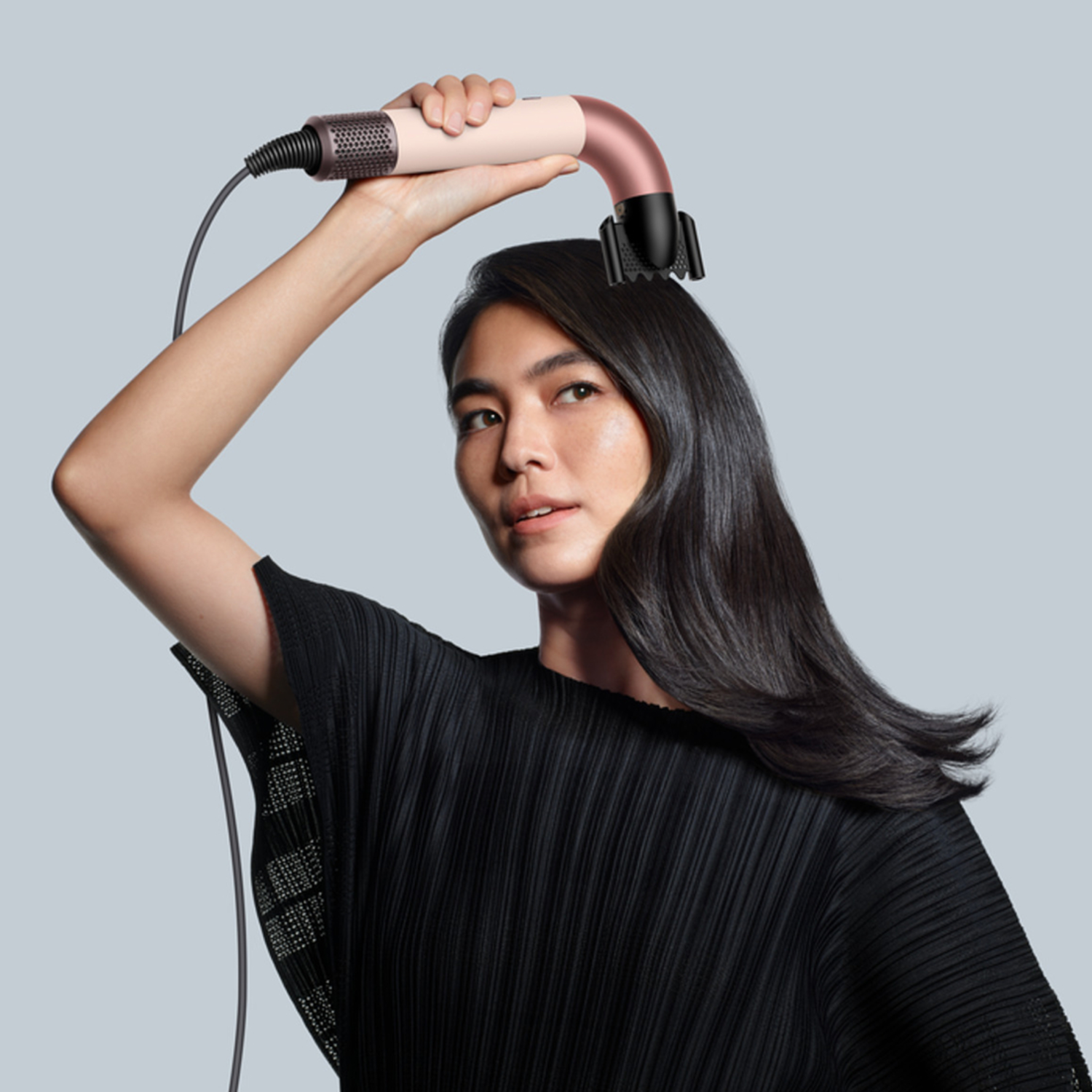 Vrouw houdt de Dyson haarstylingtool boven haar hoofd, met steil haar.