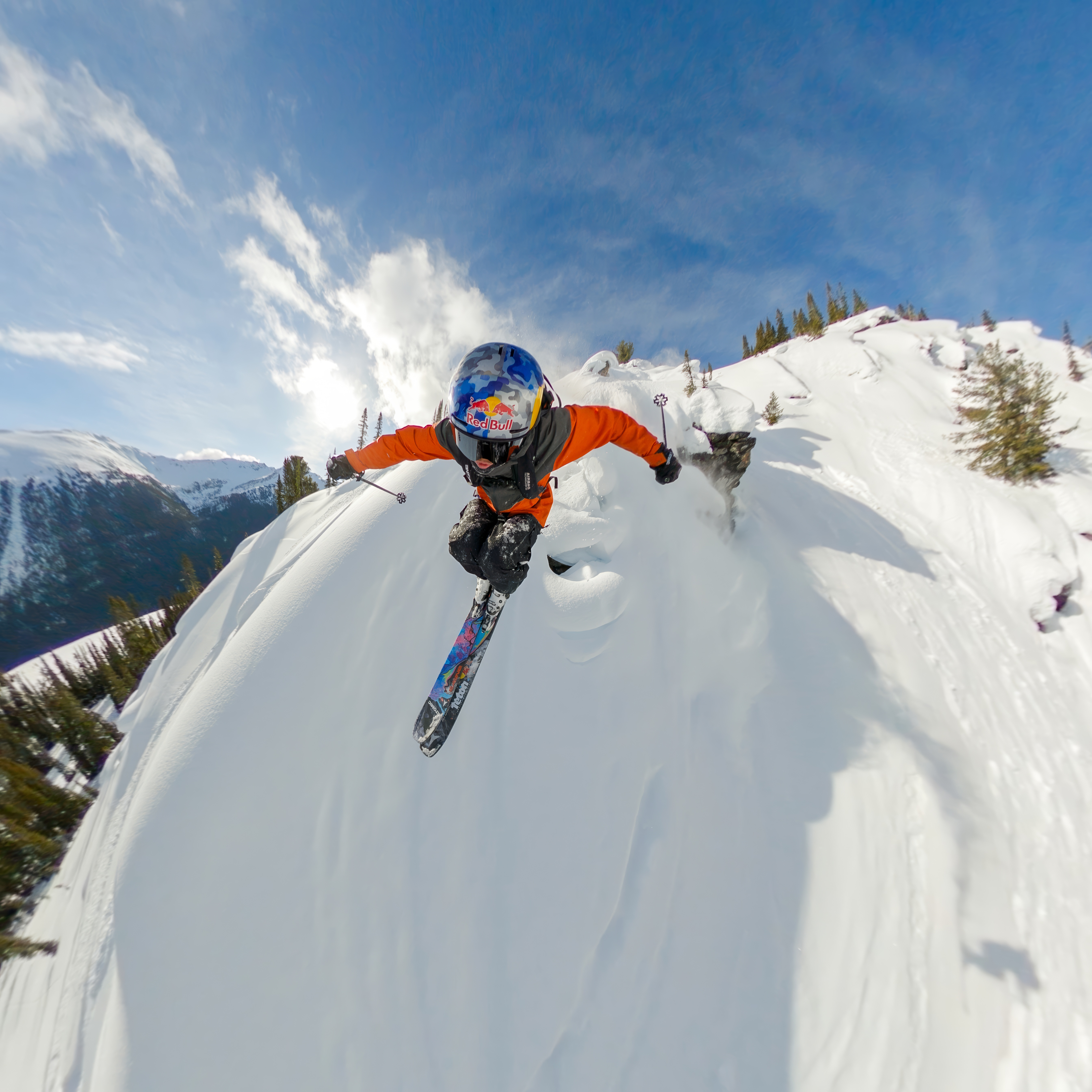 Ein Skifahrer springt von einem verschneiten Berg, der Himmel ist blau.