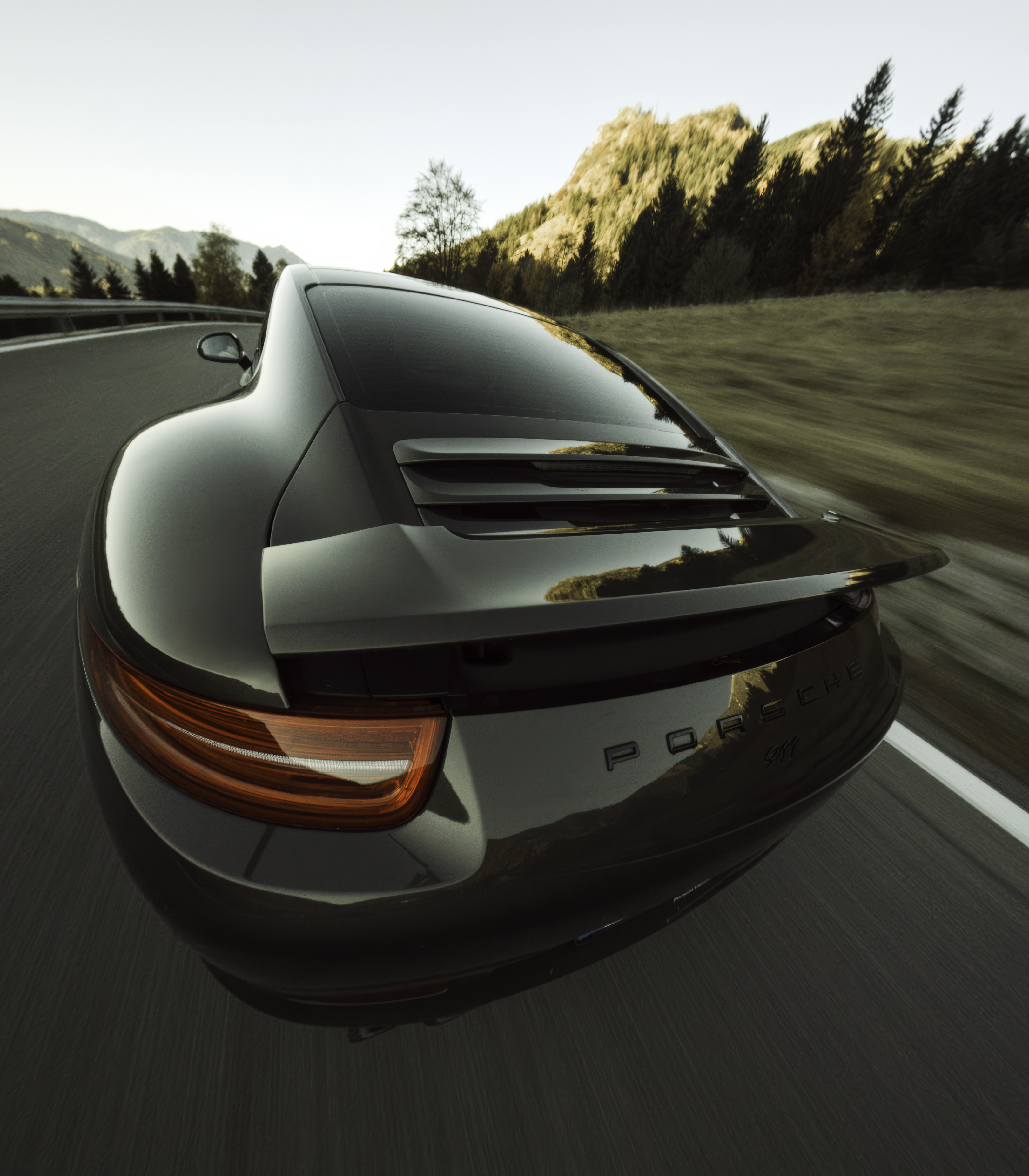 Ein dunkelgrauer Porsche-Sportwagen fährt schnell auf einer Straße mit Bergen im Hintergrund.