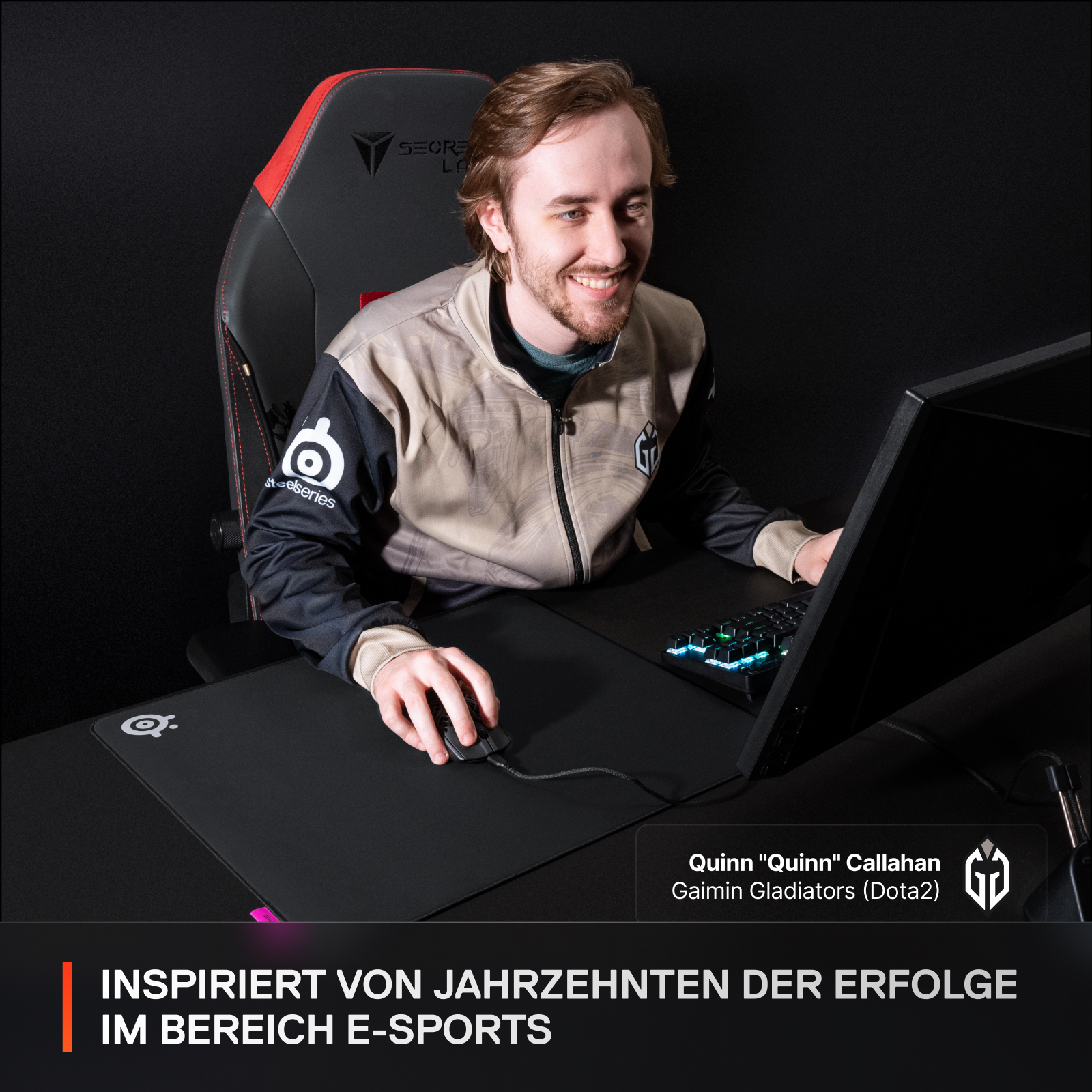 Eine Person lächelt, während sie eine Maus und Tastatur benutzt. Die Person sitzt in einem Gaming-Stuhl.