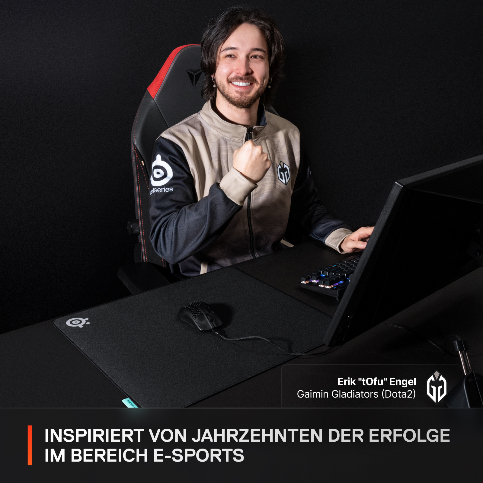 Ein lächelnder Mann in einem Gaming-Stuhl. Er hält eine Faust hoch, mit Gaming-Setup und Textüberlagerung.