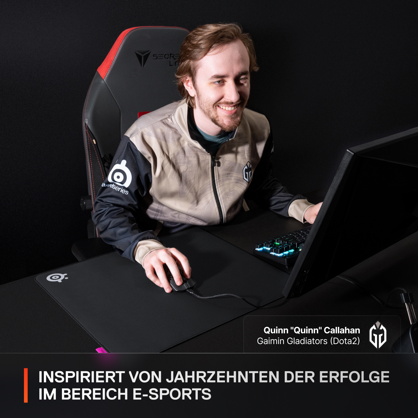 Gamer lächelt am Schreibtisch mit Maus, Tastatur, Monitor.