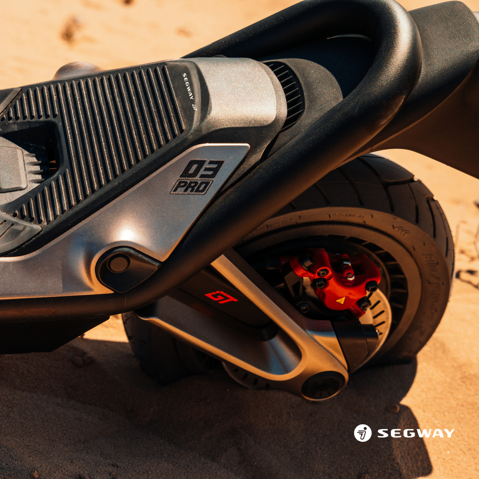 Nahaufnahme eines schwarzen und silbernen Segway-Scooter-Rads auf Sand mit roter Bremse.