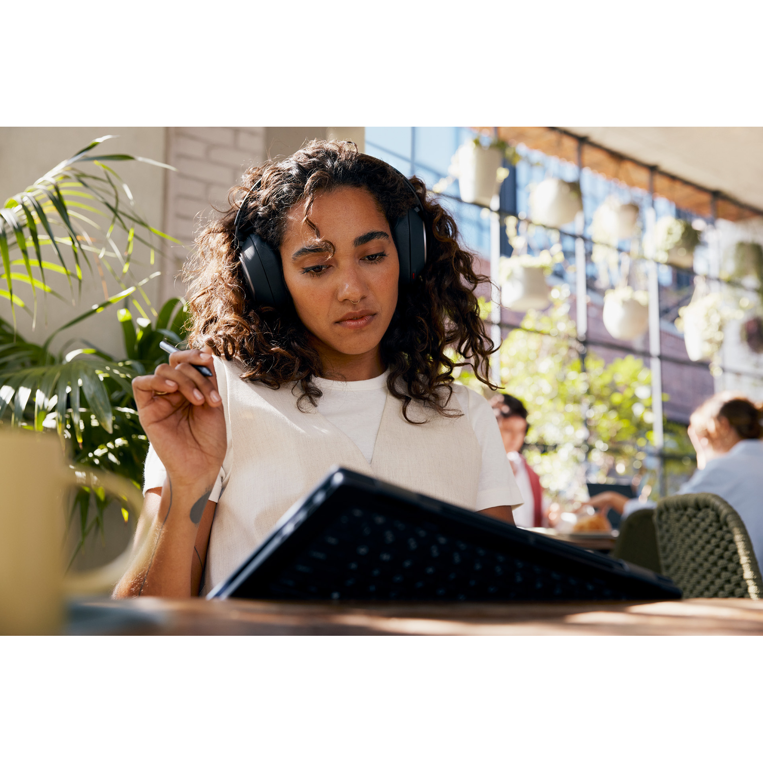 Woman wearing headphones, using a tablet with a keyboard outdoors at a cafe.