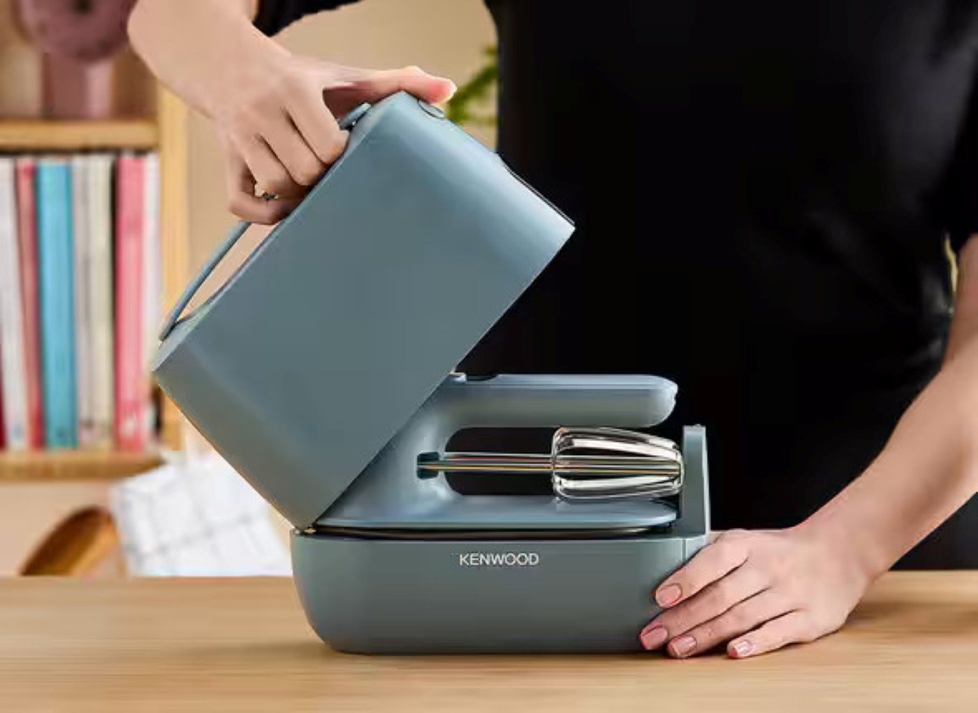 Osoba otwiera szary mikser Kenwood, drewniana powierzchnia, zbliżenie.