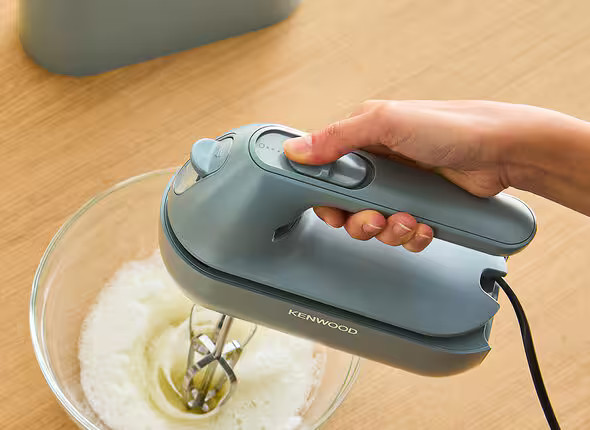 Ręka osoby trzymającej szarą ręczną mikser nad miską ubitej śmietany.