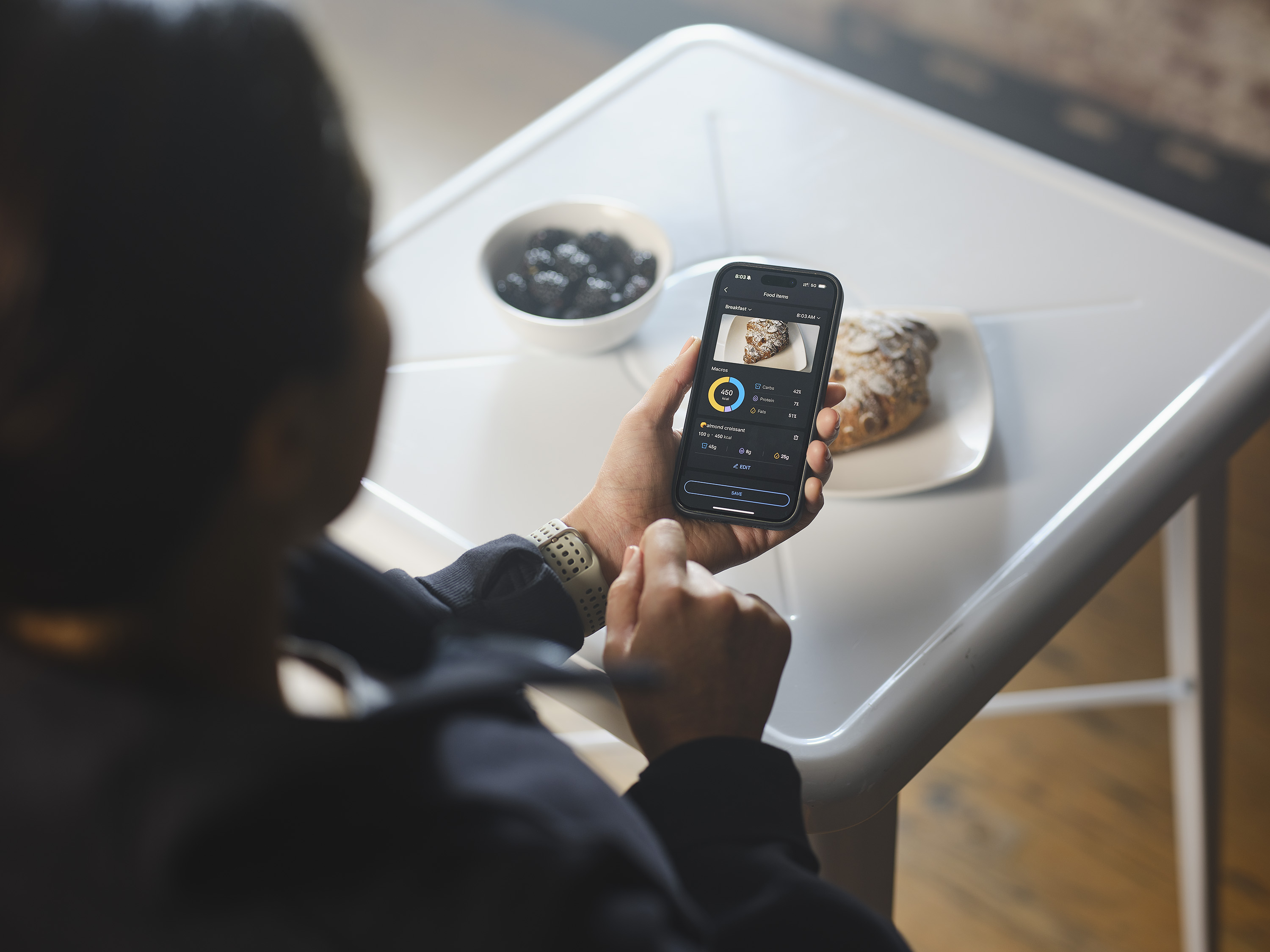 Egy fehér asztal telefonnal, egy tányér croissant-tal és egy tál. A telefon tápanyag-információkat jelenít meg.