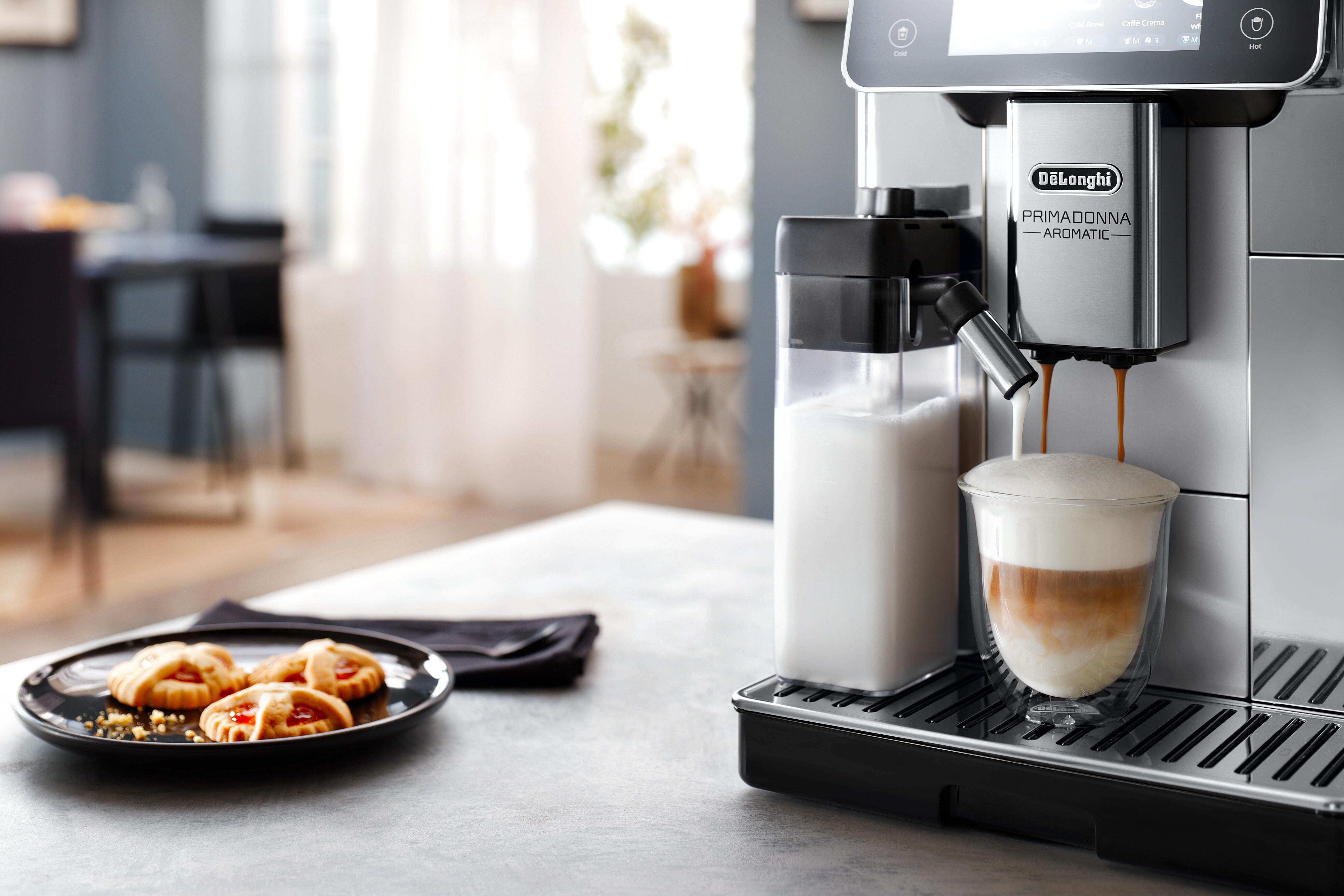 Eine Kaffeemaschine, die Kaffee zubereitet. Links ein Teller mit Keksen. Rechts eine Tasse Kaffee.