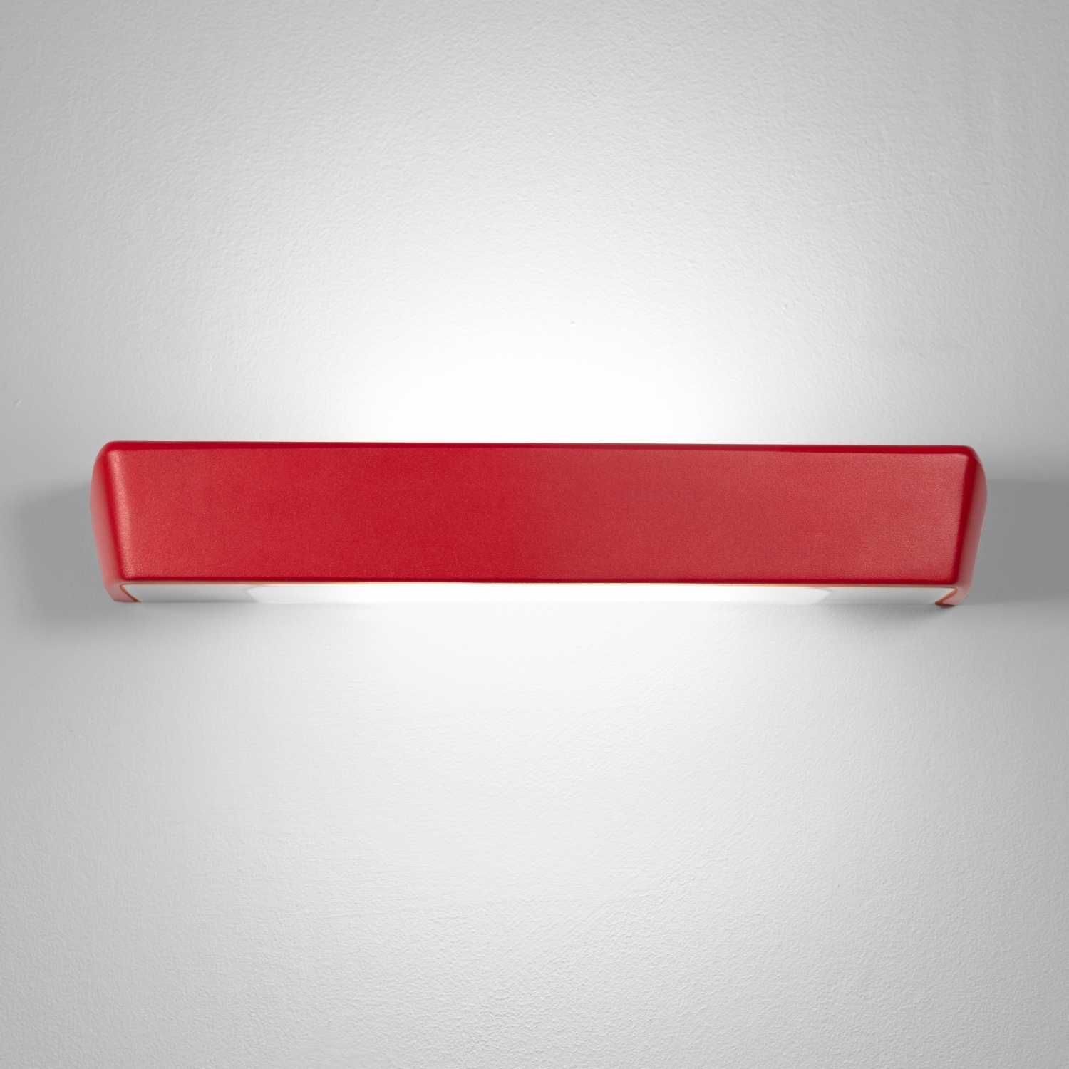 Una lampada da parete rettangolare rossa su un muro bianco, che emette luce verso il basso.