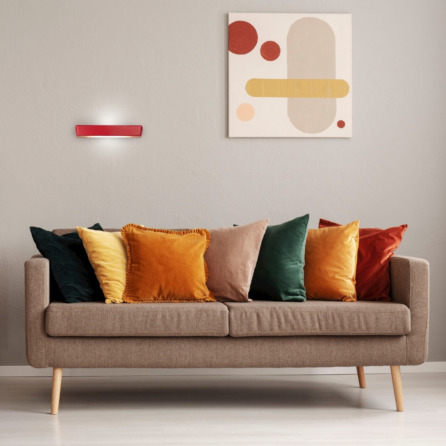 Una lampada da parete rossa sopra un divano marrone con cuscini colorati e un dipinto.