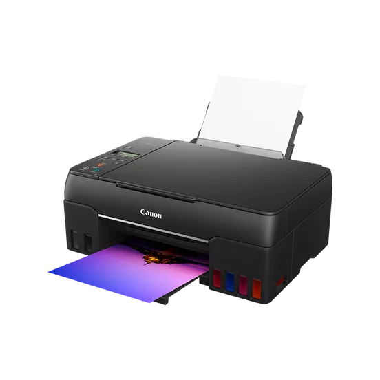 Una impresora Canon negra está imprimiendo una imagen colorida. Papel blanco en la bandeja de salida. Tanques de tinta visibles.