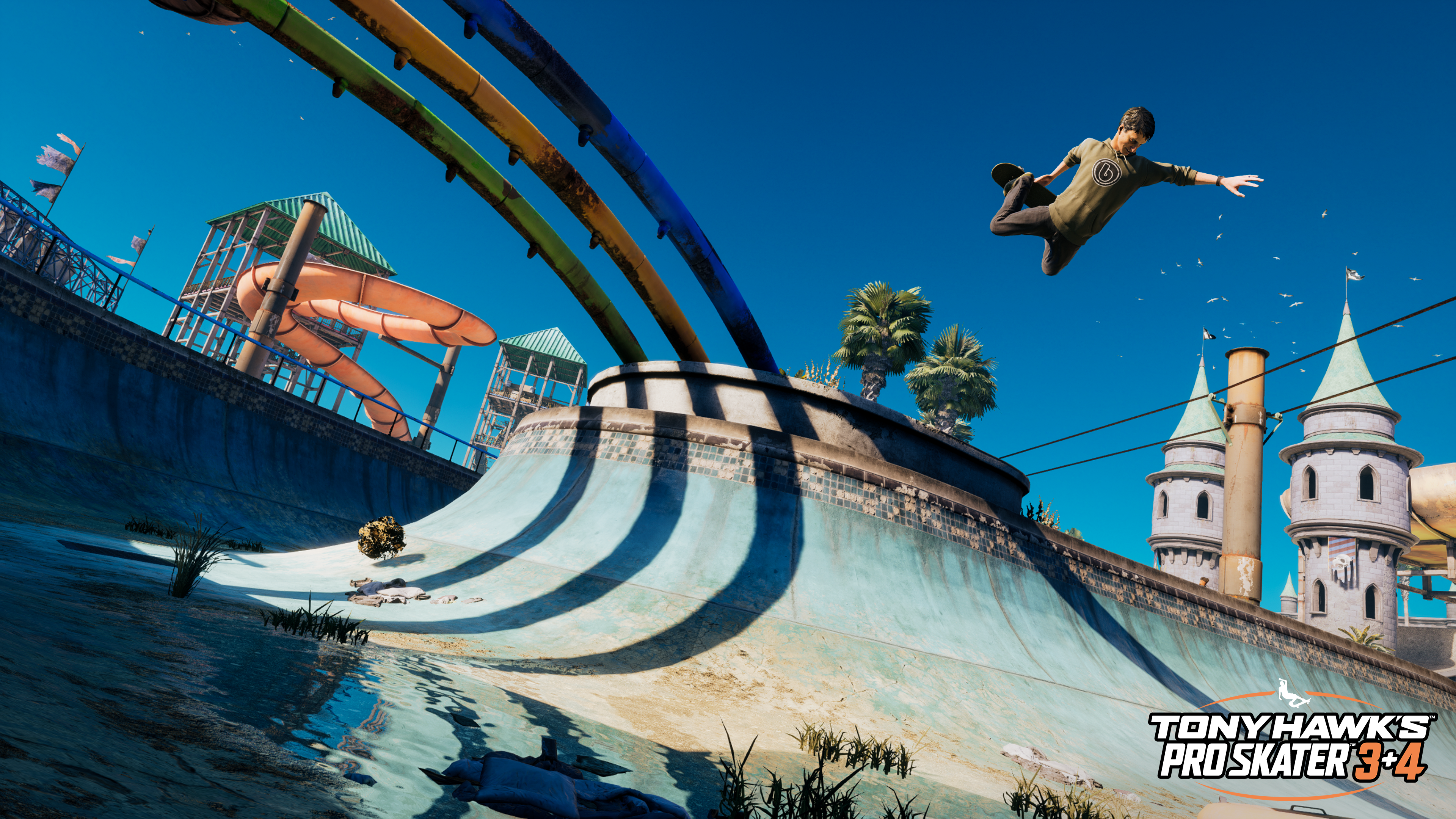 Un skateur en l'air au-dessus d'un skatepark avec toboggans et ciel bleu.